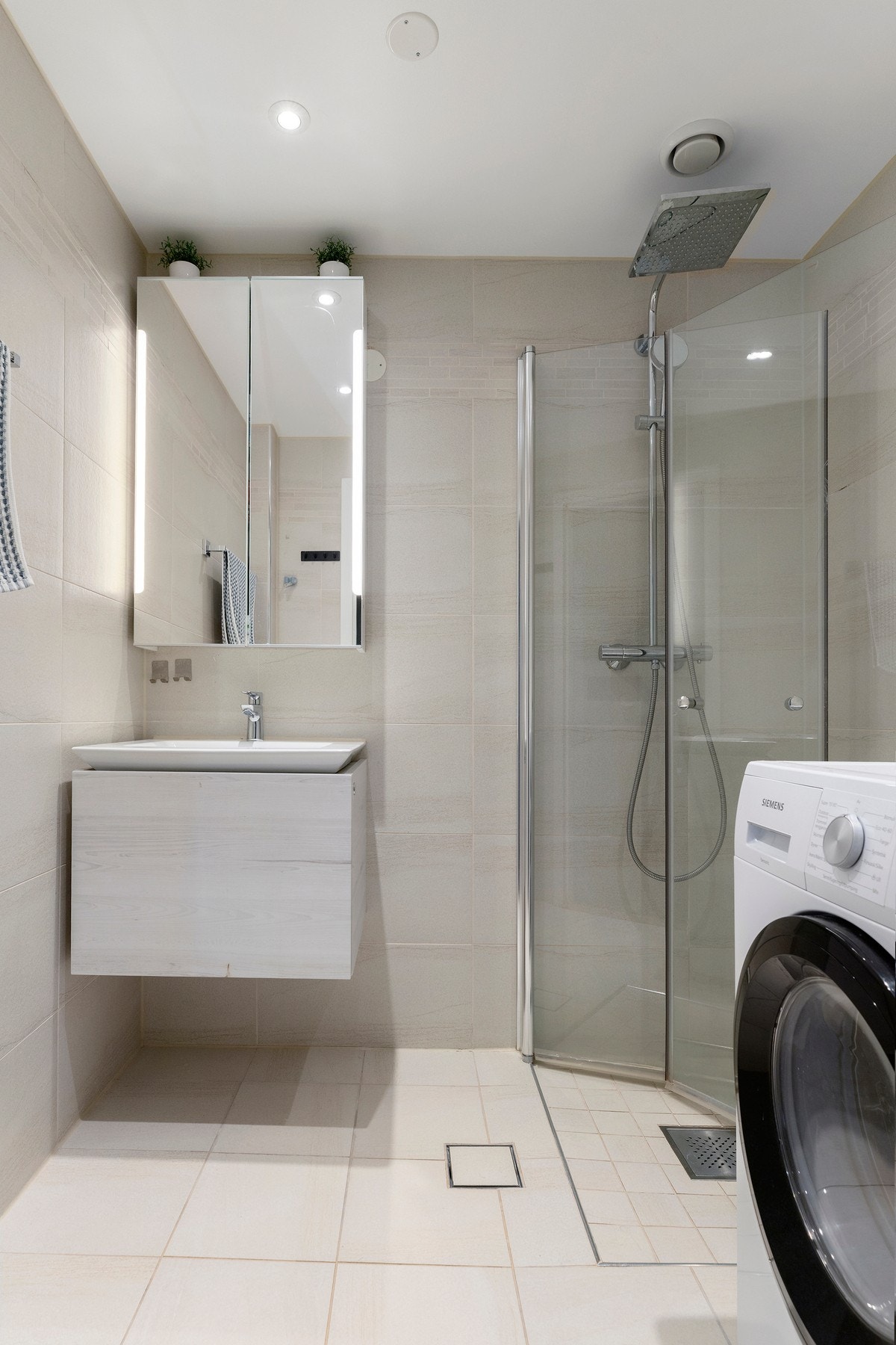 Delikat og moderne bad fra 2019 med flislagte overflater, varmekabler og innfelte spotter. Badet har dusjhjørne med glassdører, moderne servantinnredning og opplegg for vaskemaskin. Galleribilde