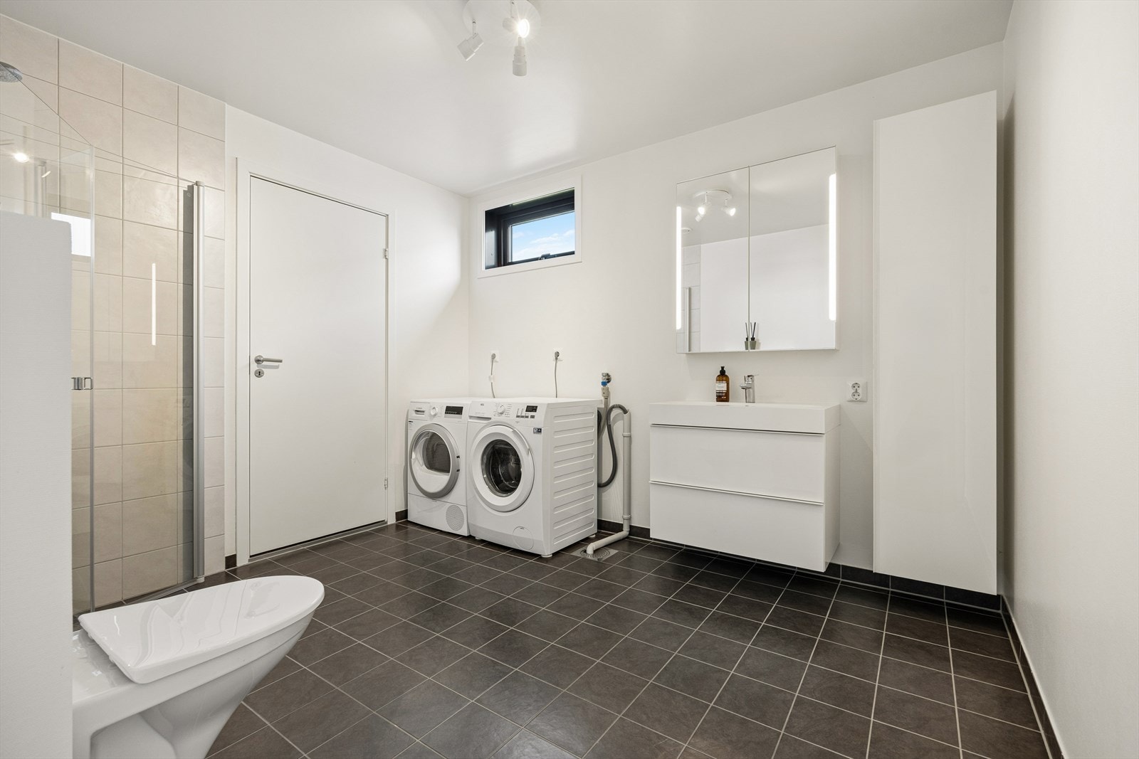 Praktisk bad/vaskerom i 1. etasje har flislagt gulv med vannbåren varme. Badet er utstyrt med toalett, badekar, flislagt dusjhjørne
med glassvegger, innredning med servant og speilskap, samt opplegg for vaskemaskin. Galleribilde