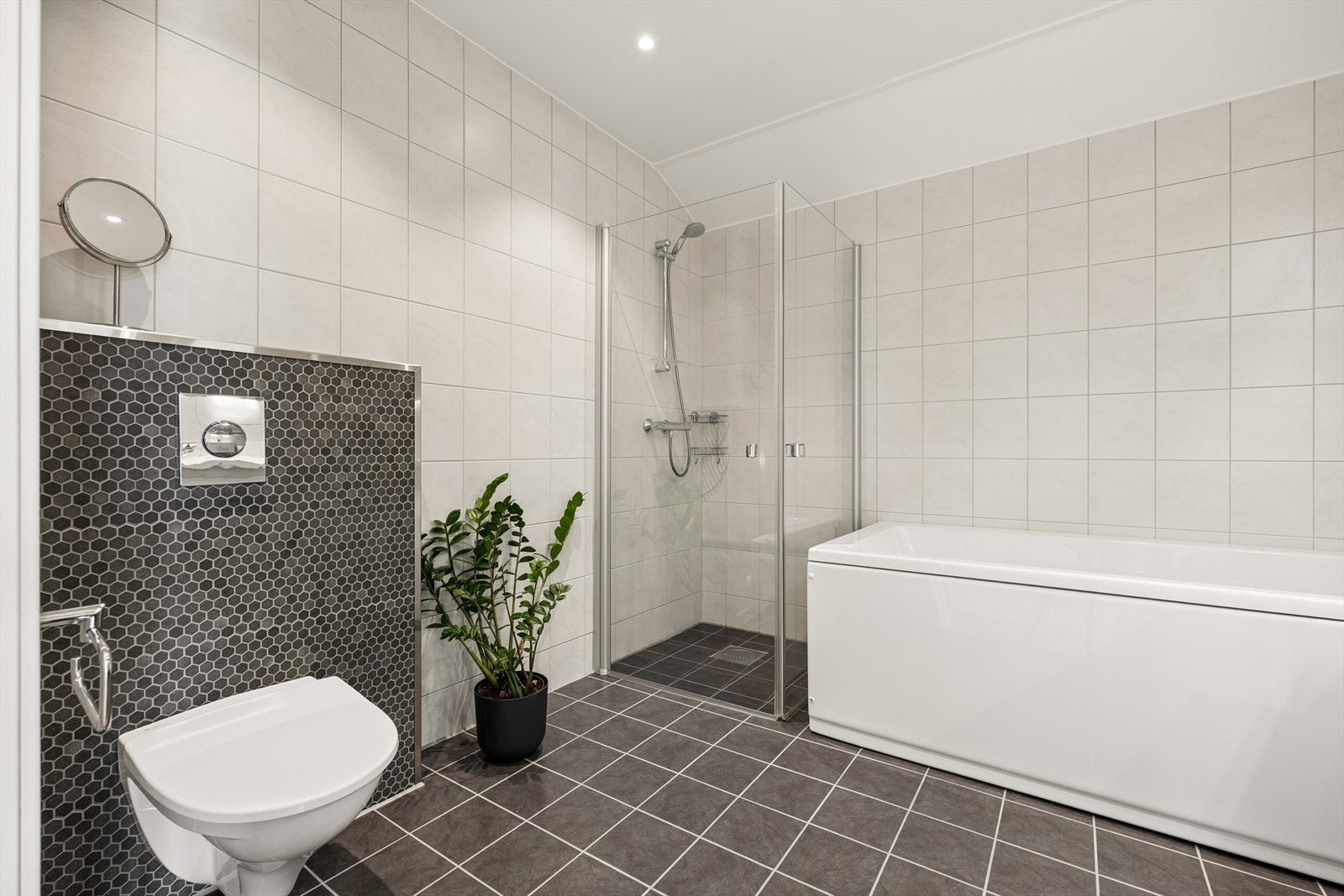 Badet er utstyrt med veggmontert toalett, badekar, dusjhjørne med glassvegger, samt baderomsinnredning med servant og speilskap. Galleribilde