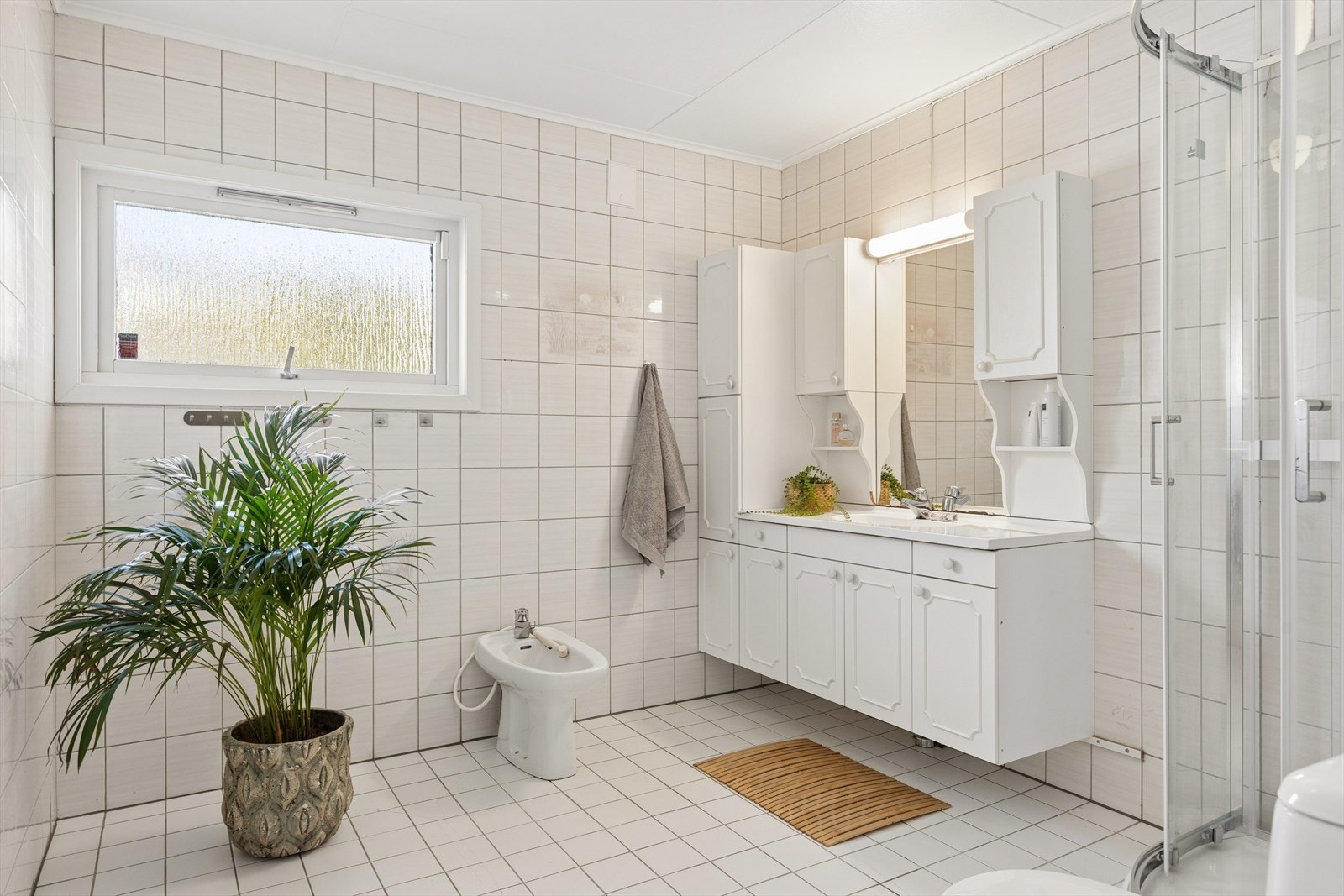 Helfliset bad med varme i gulv. Rommet er innredet med baderomsinnredning med nedfelt servant, dusjkabinett, gulvmontert toalett og bidè. Galleribilde