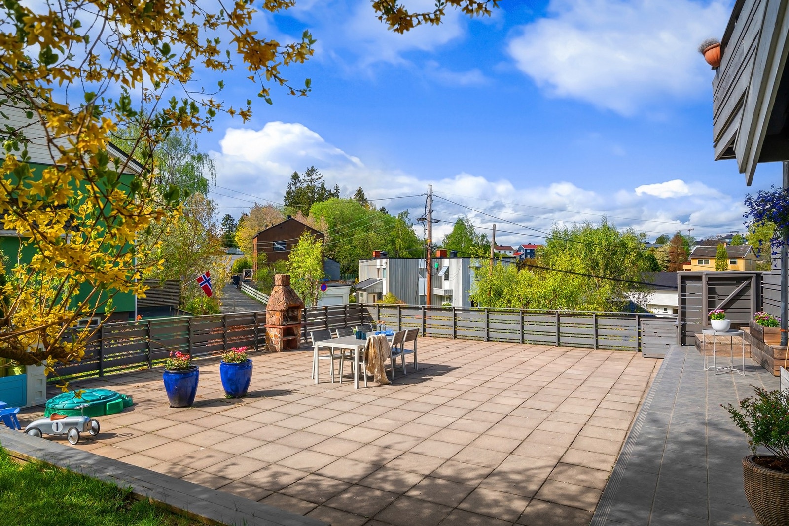 Fra hoveddelen er det utgang til en solrik terrasse på 28 kvm, med videre adkomst til en stor felles terrasse som overbygger garasjene i sameiet og en nydelig hage som omkranser bygget. Galleribilde