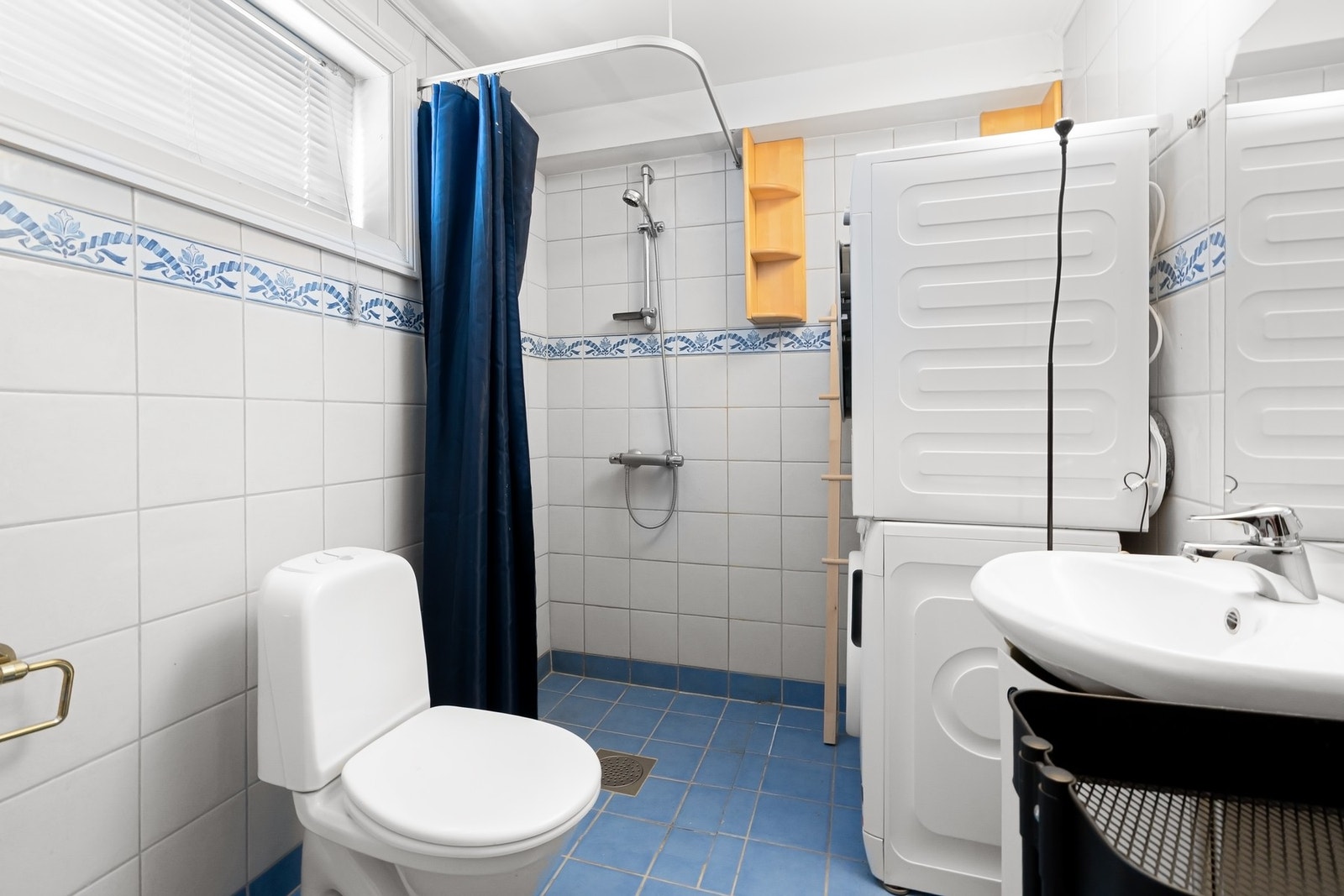 Badet i hybelen er utført med blå gulvfliser, hvite veggfliser, gulvvarme og vindu, samt opplegg for vaskemaskin og tørketrommel i søyleløsning. Innredningen består av servant på hvitt skap, speil, et toalett og et åpent dusjhjørne med stang til forheng. Galleribilde