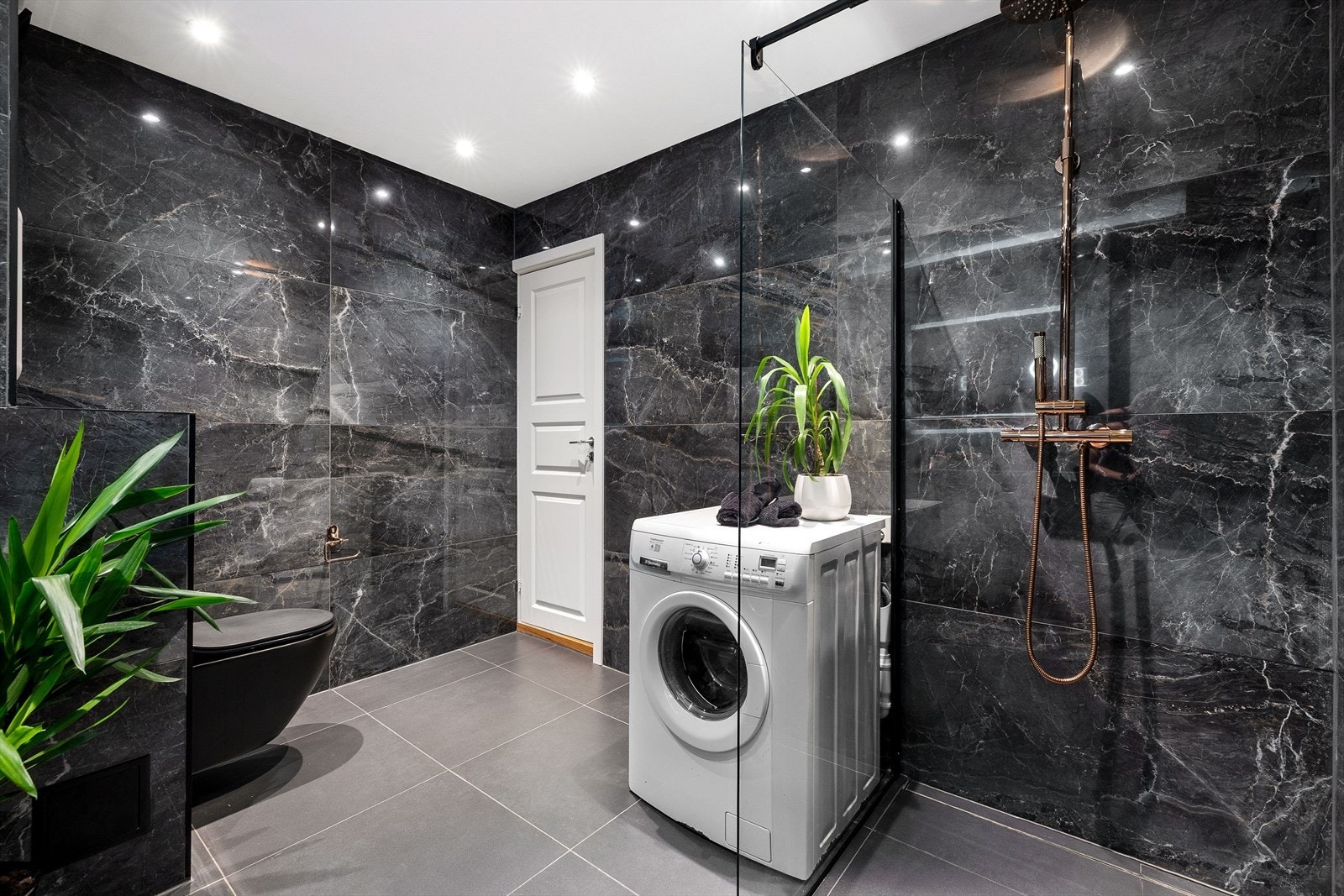 Badet er innredet med vegghengt toalett, dusjhjørne med glassvegg, servant med tilhørende innredning og opplegg for vaskemaskin. Galleribilde