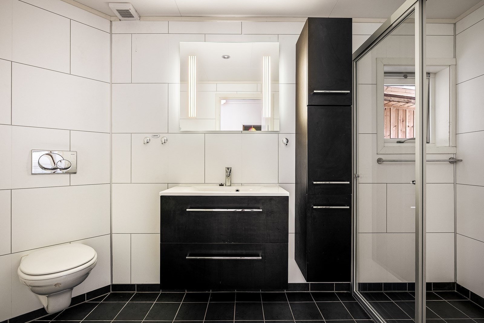 Badet er innredet med vegghengt toalett, servant med møblement, speil med belysning og downlights i taket. Galleribilde