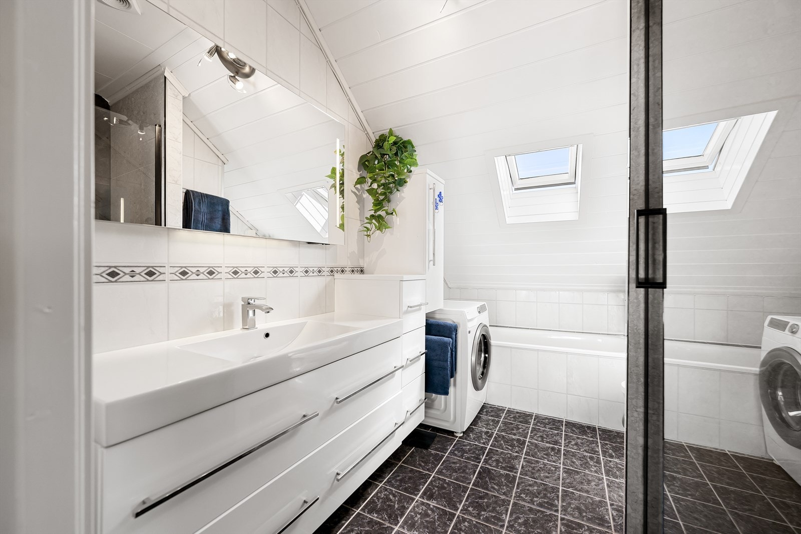Badet ble oppgradert med mørke gulvfliser i 2012 og har ellers flisplater på veggene, gulvvarme og hvitmalt panelhimling Galleribilde