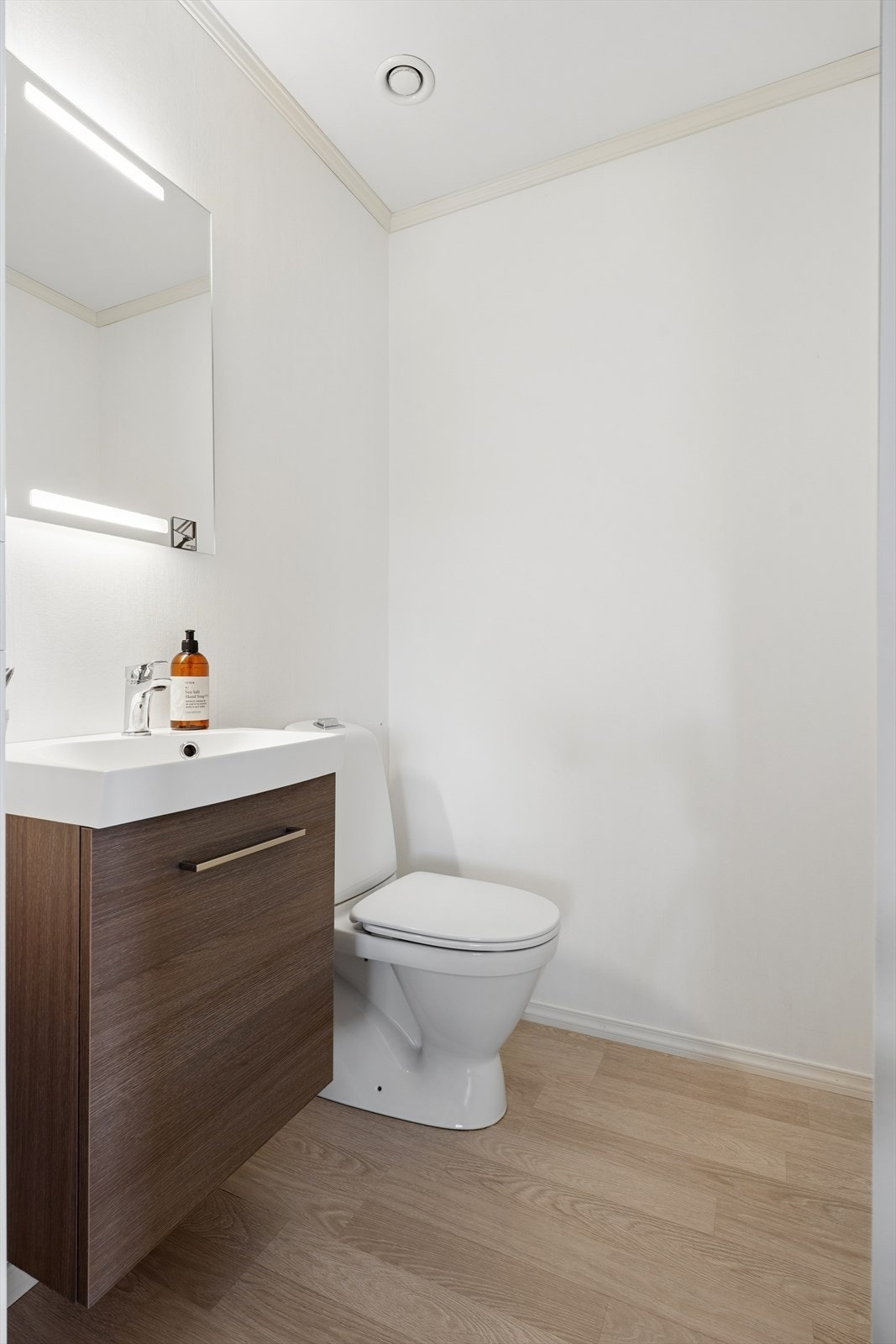 Praktisk wc rom med klosett, servantinnredning med installert vannstoppsystem og speil med integrerte ledlys. Galleribilde