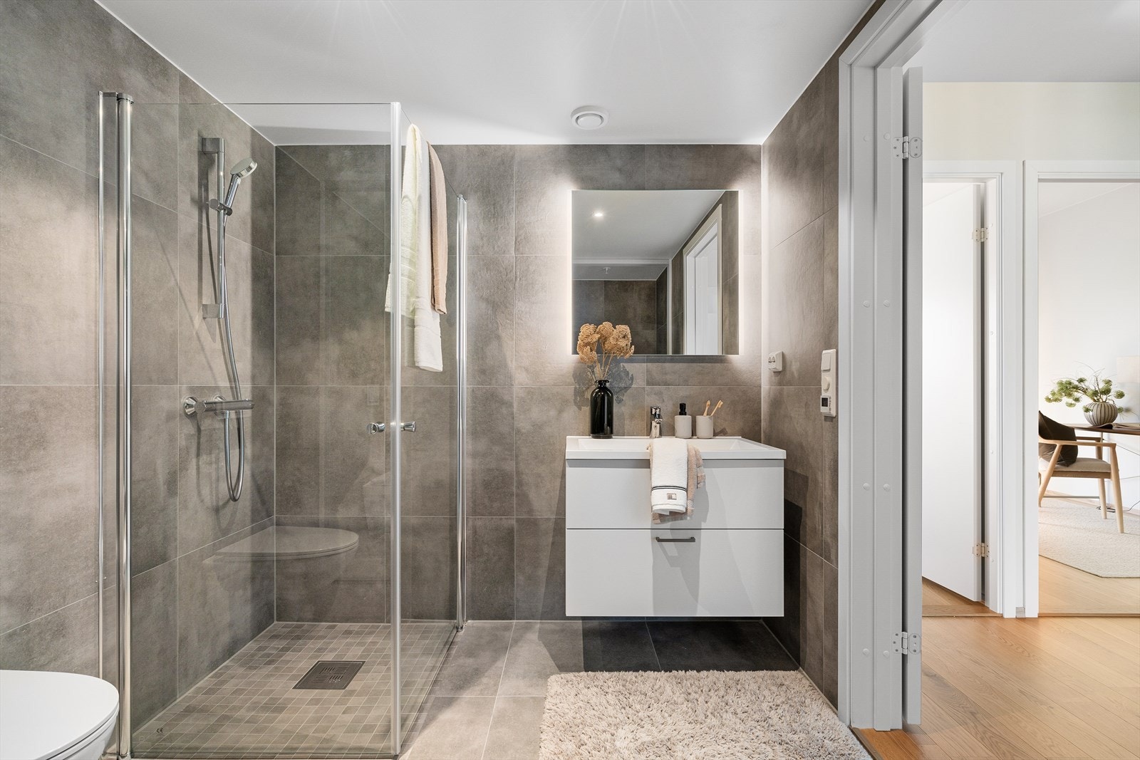 Badet fremstår romslig og funksjonelt med dusjsone i glass, vegghengt innredning og gode oppbevaringsmuligheter. Galleribilde