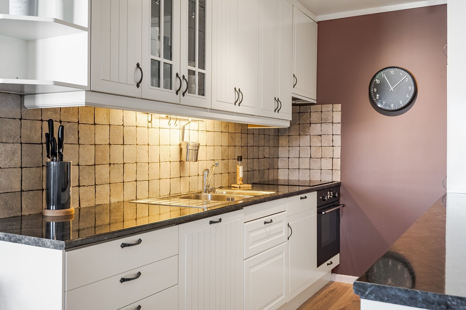 Innredningen har lyse profilerte fronter og laminert benkeplate med nedfelt oppvaskkum. Praktisk med fliser i benkeryggen og belysning under de takhøye overskapene. Galleribilde
