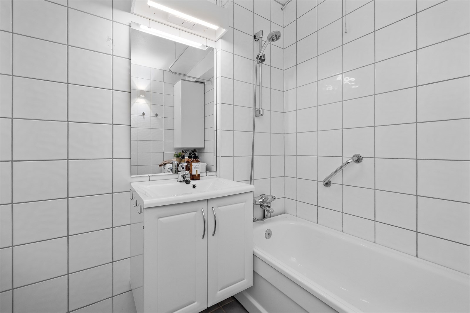 Flislagt bad med servantinnredning, speil med belysning og badekar med dusjopplegg. Galleribilde