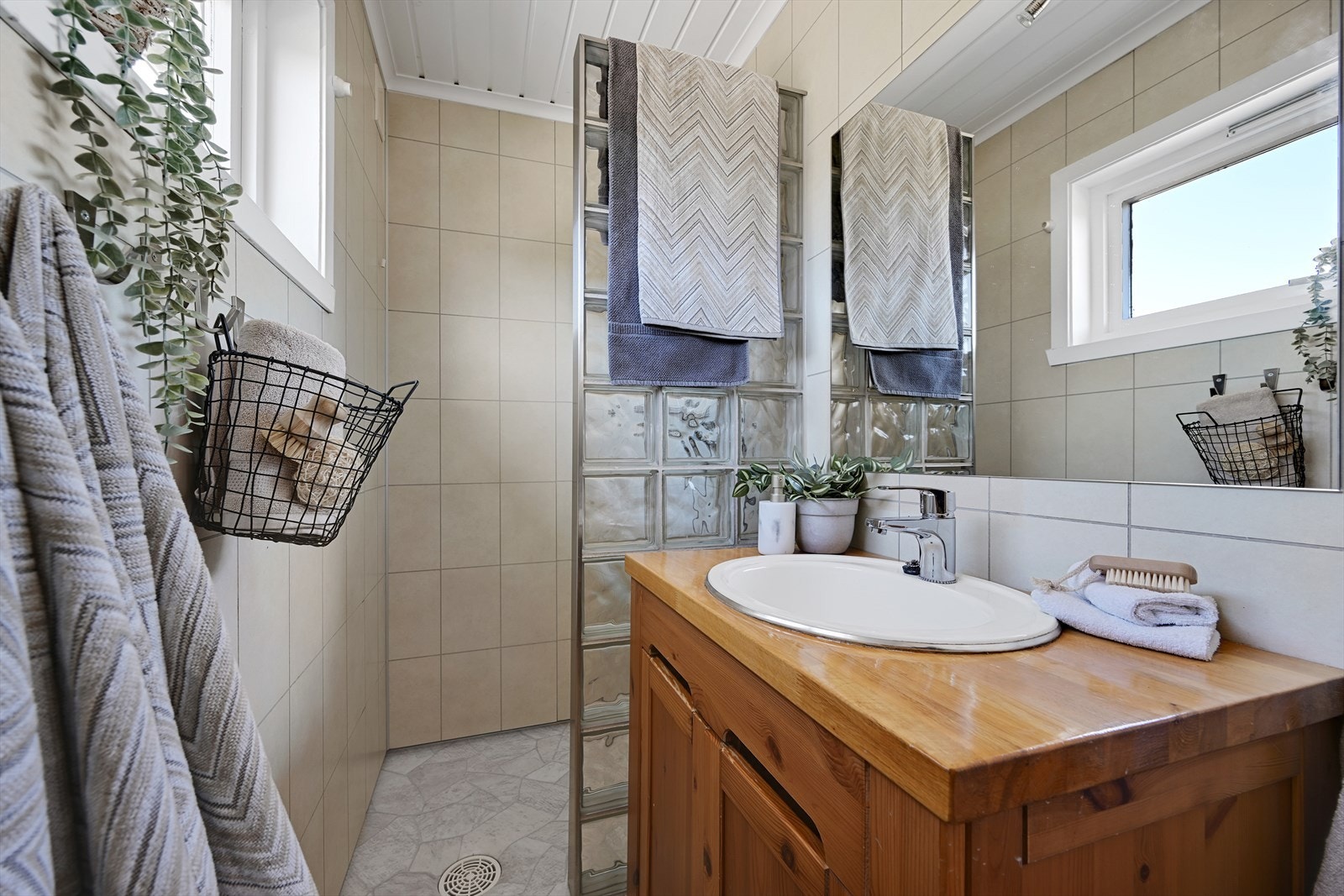 Badet er innredet med servant i baderomsmøbel, toalett og dusj på vegg med vegg av glassbyggerstein. Galleribilde