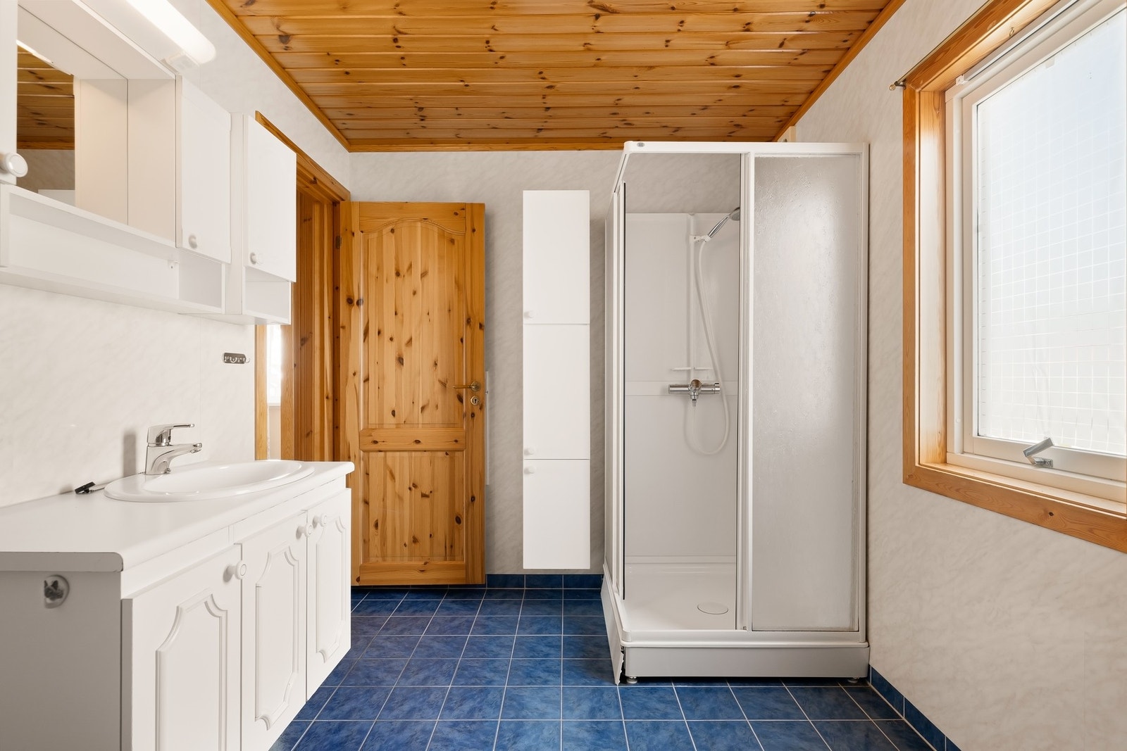 Badet er utstyrt med gulvstående wc, stor baderomsinnredning, dusjkabinett, utslagsvask og opplegg for vaskemaskin Galleribilde