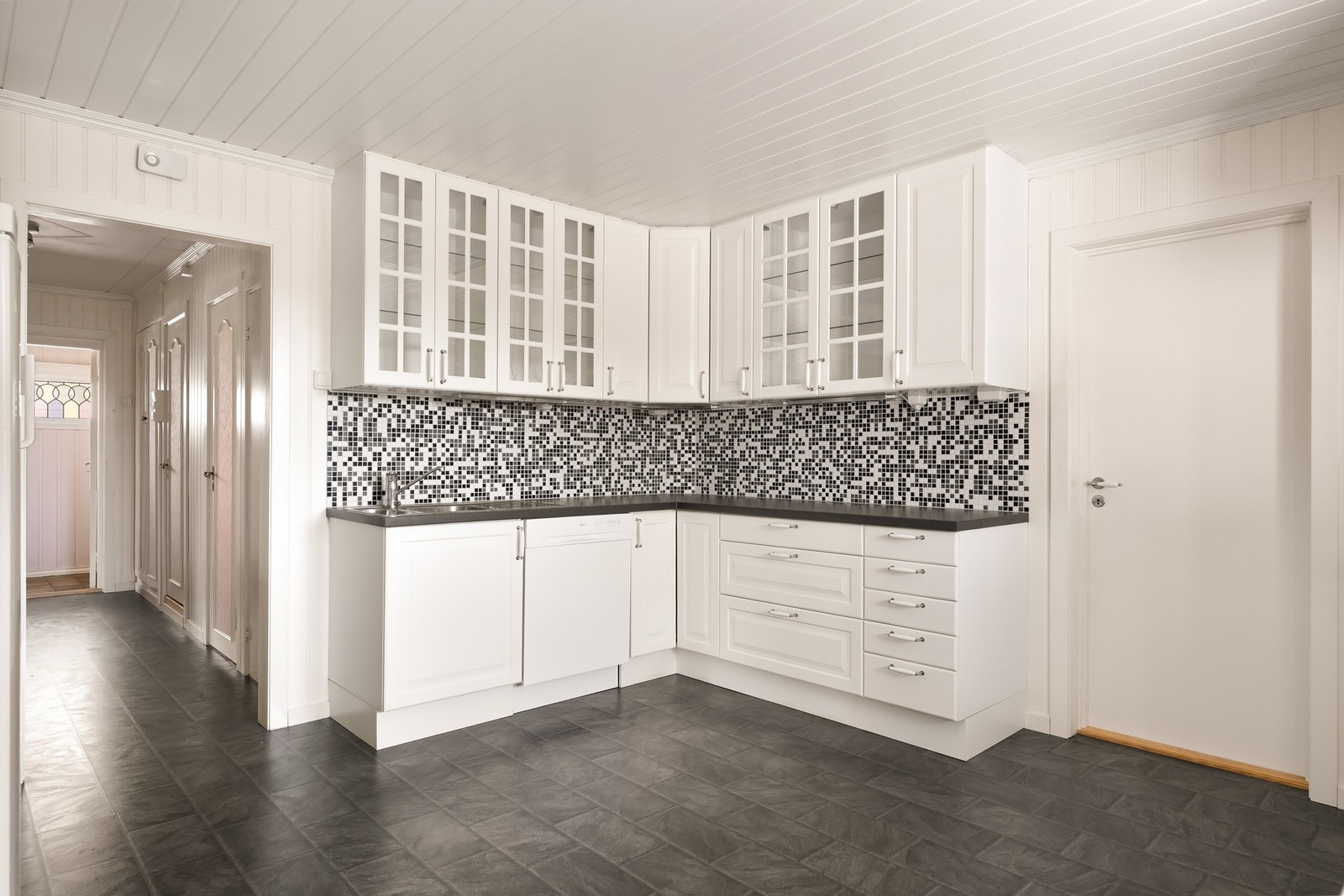 Innredningen har hvite profilerte fronter, mørk laminert benkeplate og mosaikkfliser mellom kjøkkenbenk og overskap Galleribilde