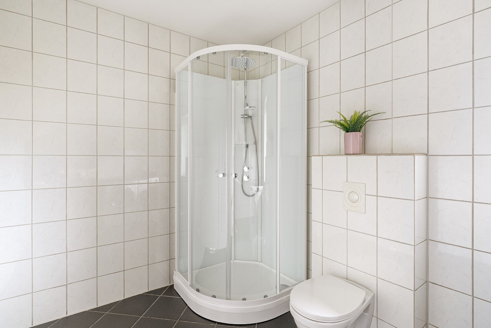 Badet er utstyrt med dusjkabinett (2025), vegghengt toalett, servant i baderomsinnredning og tilkobling for vaskemaskin og tørketrommel. Galleribilde