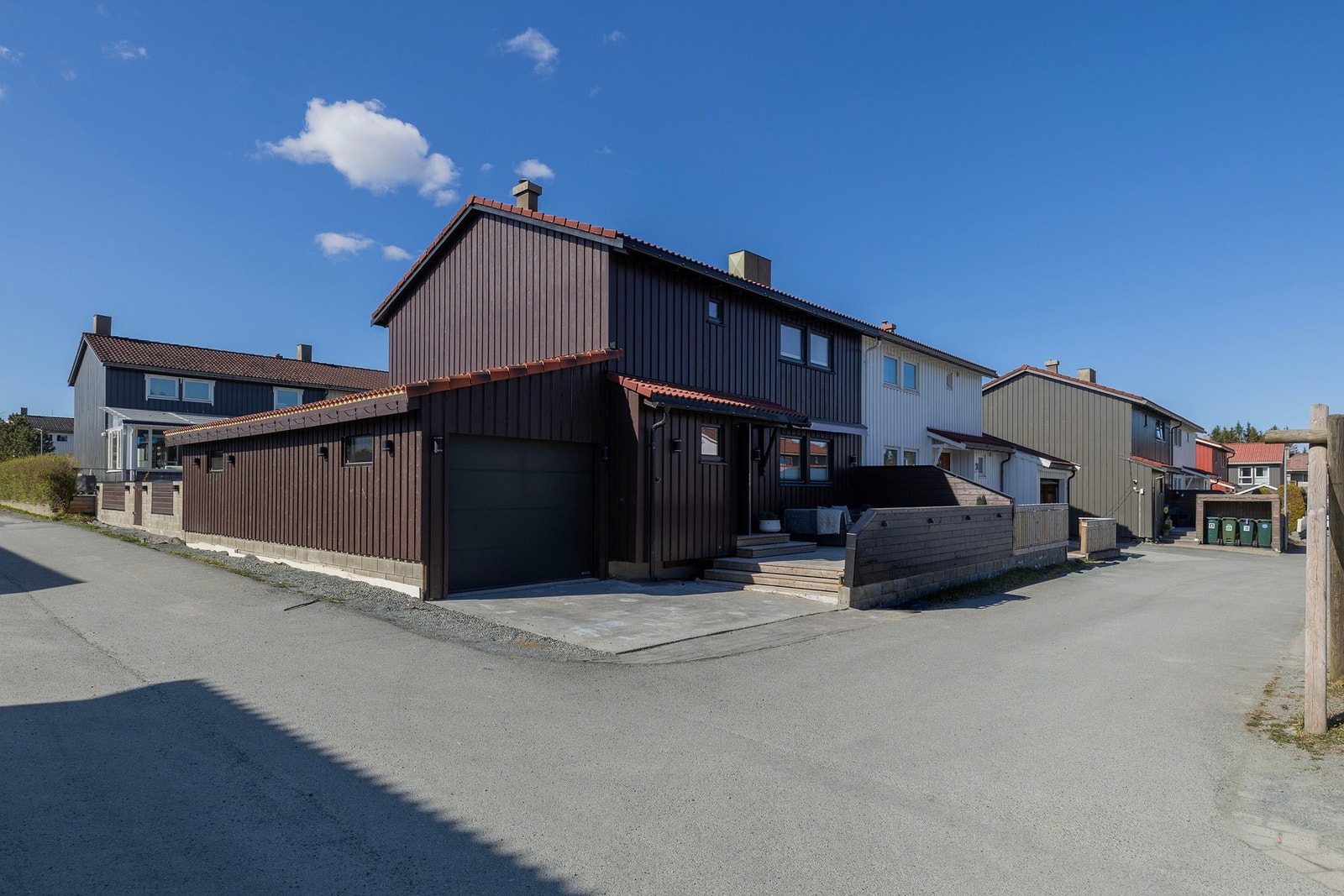 Fasade fremside. Romslig garasje med leddport. Steinlagt parkeringsplass, solterrasse ved inngangsparti. Galleribilde