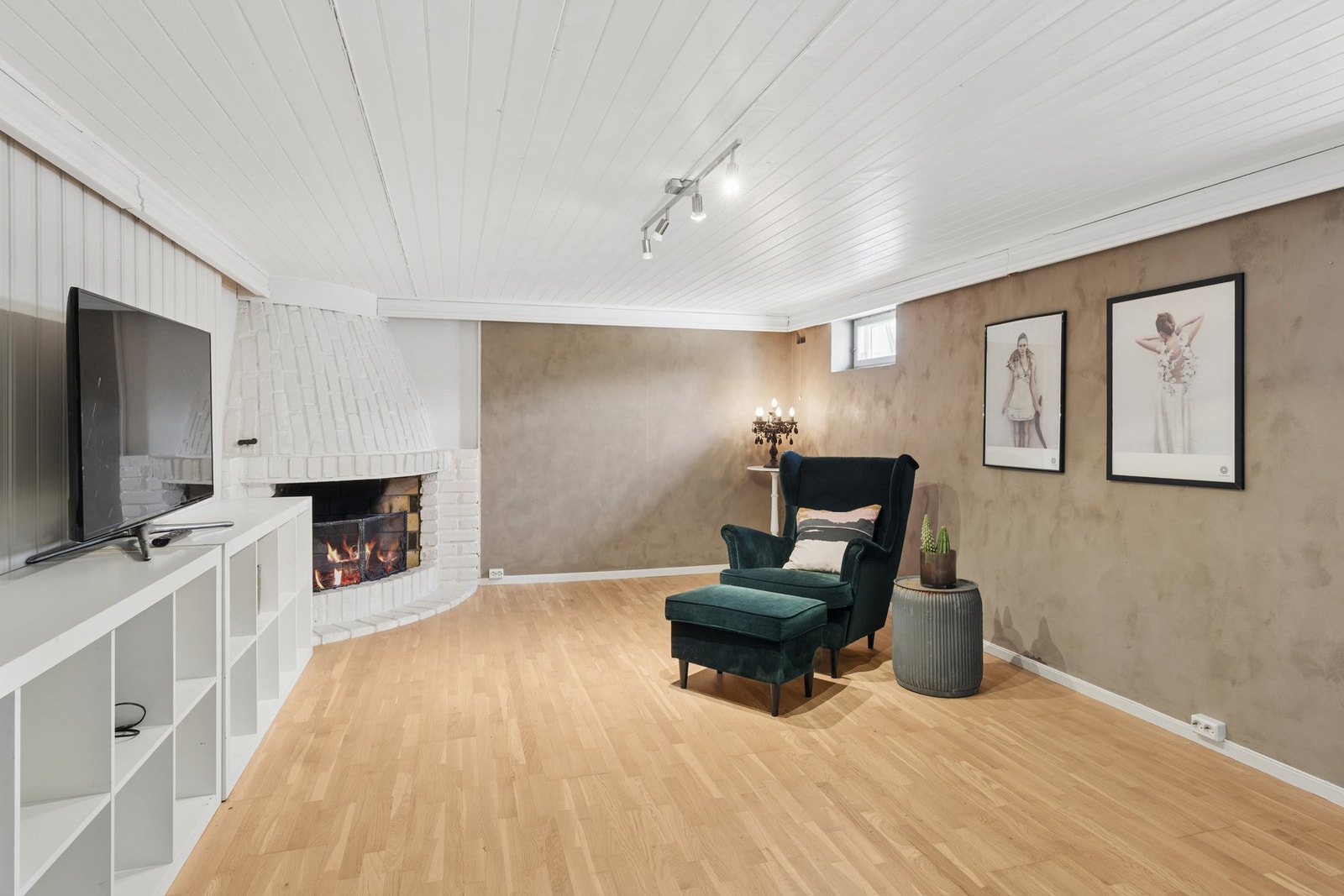 Kjellerstuen er av god størrelse, rommet er holdt i duse farger som står godt til parkettgulvet, og i et hjørne er det en oppmurt, åpen peis for ekstra hygge Galleribilde