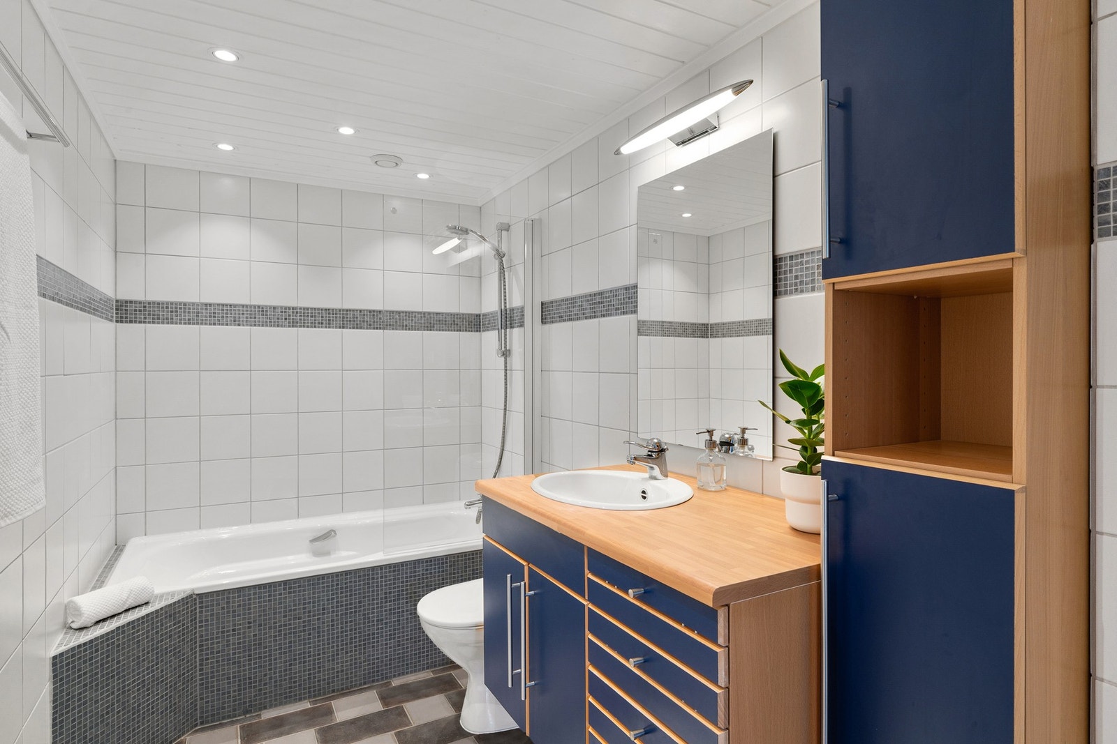 Badet har en romslig utforming med flislagte overflater, badekar med dusjløsning, servant med god skapplass og toalett. Galleribilde