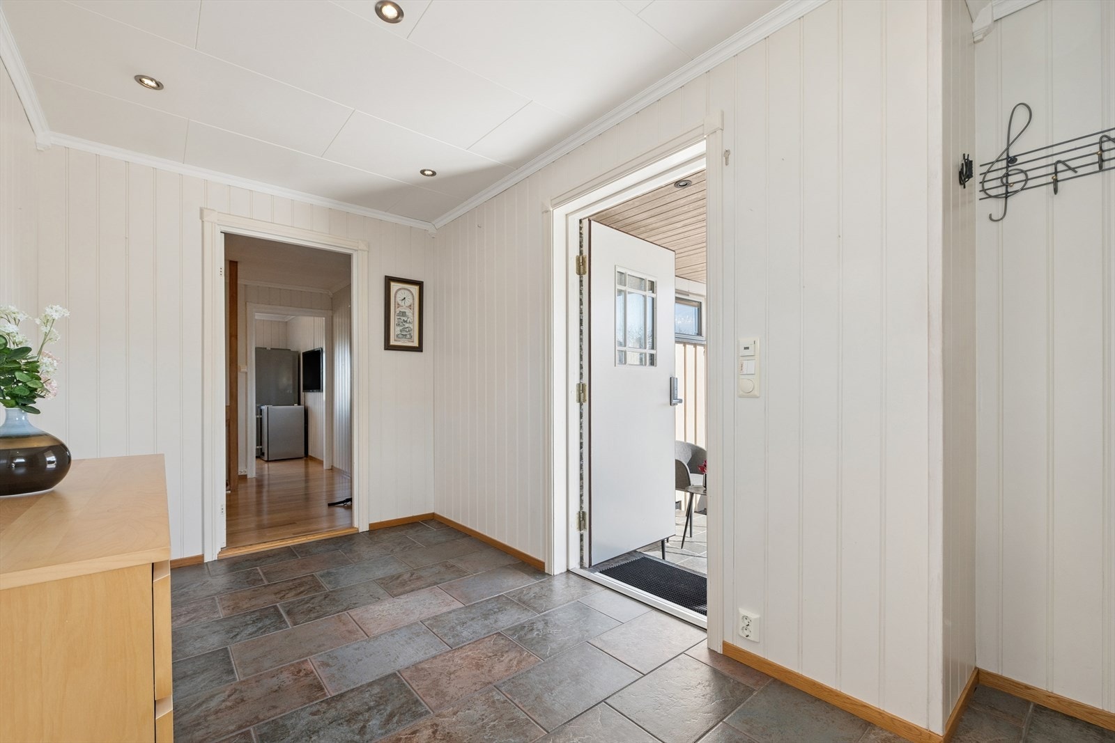 Velkommen inn i en lys og tiltalende enebolig med fin standard, spennende planløsning og et sosialt, familievennlig areal. Ytterdøren har glassfelt, og entréen er utført med lysmalt panel på veggene, panel i taket og flislagt gulv med varmekabler. Galleribilde