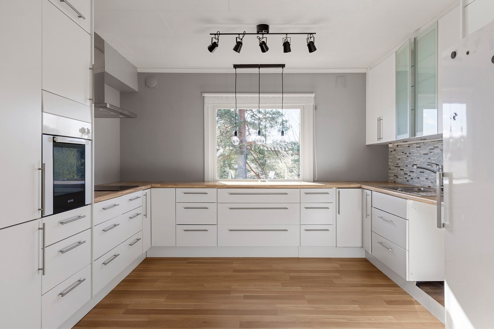 Stort kjøkken med god skap- og benkeplass. Benkeskap og overskap med folierte skrog og slette hvite fronter.Laminat benkeplate med nedfelt oppvaskkum av metall. Ventilatorhette med avtrekk. Integrert induksjonstopp og stekeovn. Opplegg for oppvaskmaskin. Galleribilde