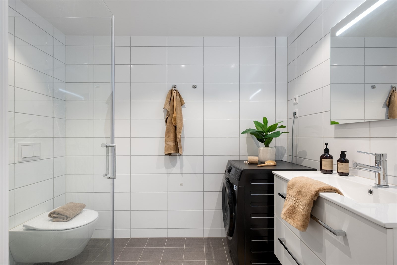 Pent helfliset bad innredet med baderomsinnredning med servant, vegghengt toalett, dusj og opplegg for vaskemaskin. Galleribilde