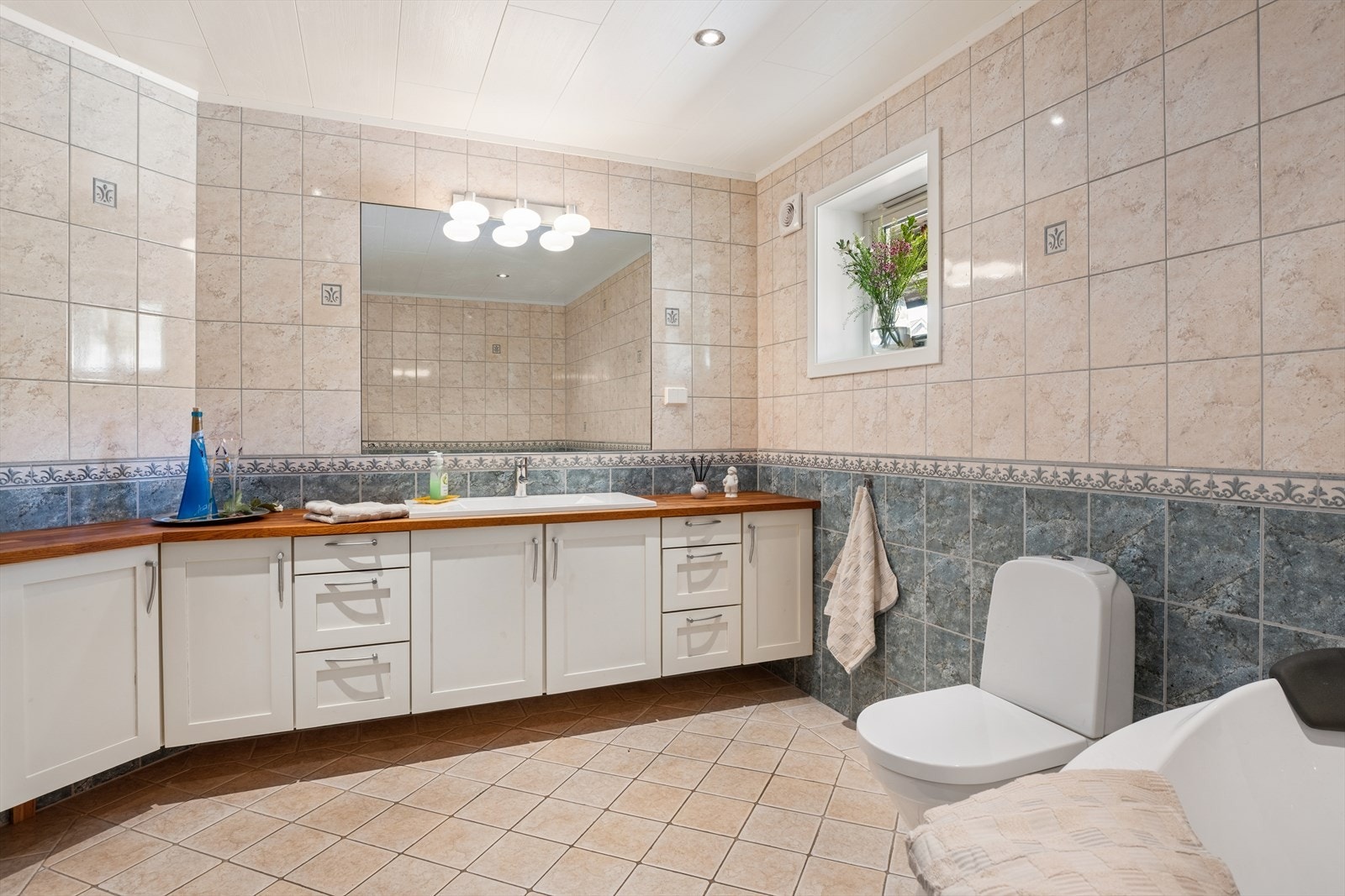 Badet har fliser på gulv og vegger, vannbåren gulvvarme og en bred servantinnredning. Galleribilde