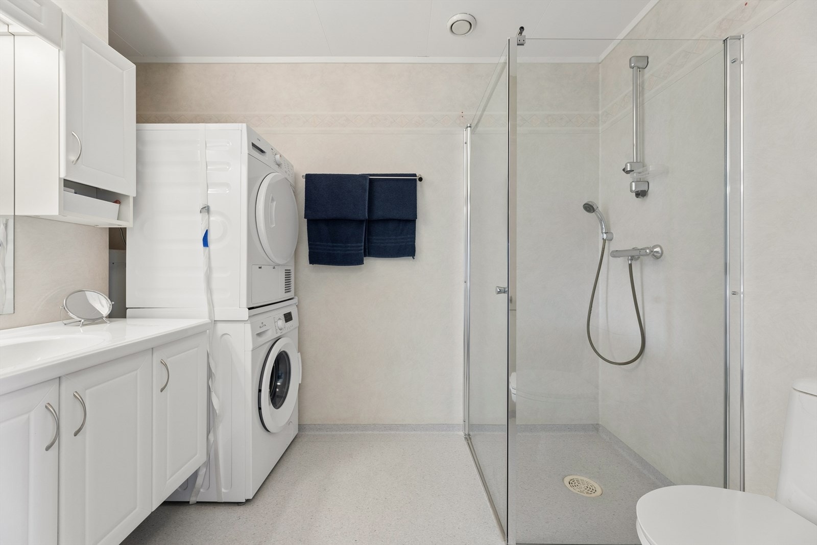 Badet er kombinert bad og vaskerom, og har elektriske varmekabler i gulvet. Rommet er utstyrt med toalett, dusjhjørne med glassvegger og servantinnredning. Galleribilde