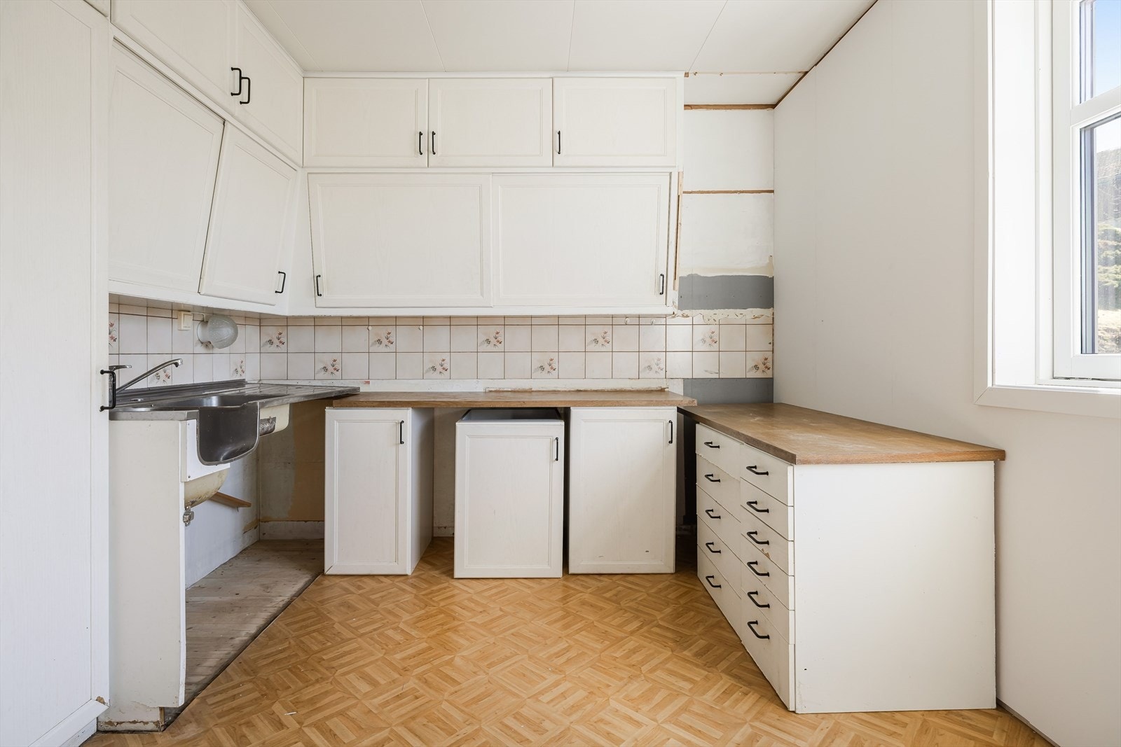 Kjøkkenet har eldre innredning med profilerte fronter, benkeplater i laminat og oppvaskkum i rustfritt stål. Galleribilde
