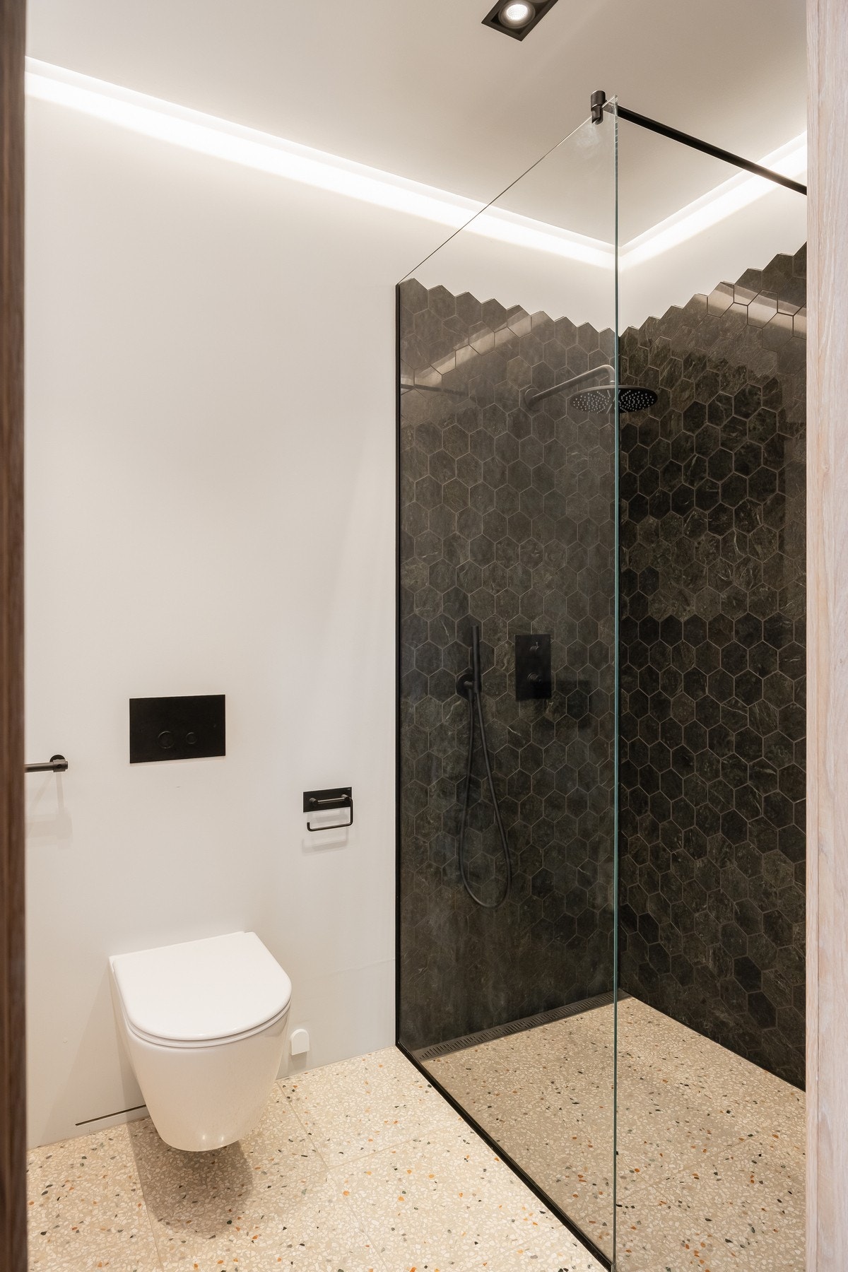 Badet har terrazzofliser på gulv og flislagt dusjnisje. Her er baderomsinnredning, vegghengt toalett og stor dusjnisje. Galleribilde