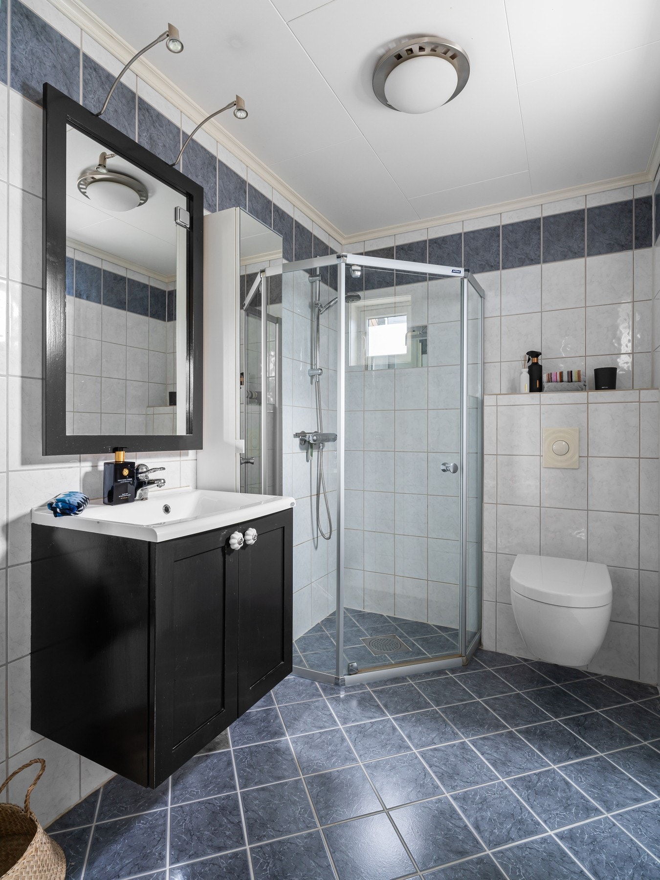 Boligen har totalt tre bad, et i hver etasje. Badet i første etasje har fliser på både gulv og vegger. Badet er innredet med servantskap, speil, dusj og toalett. Galleribilde