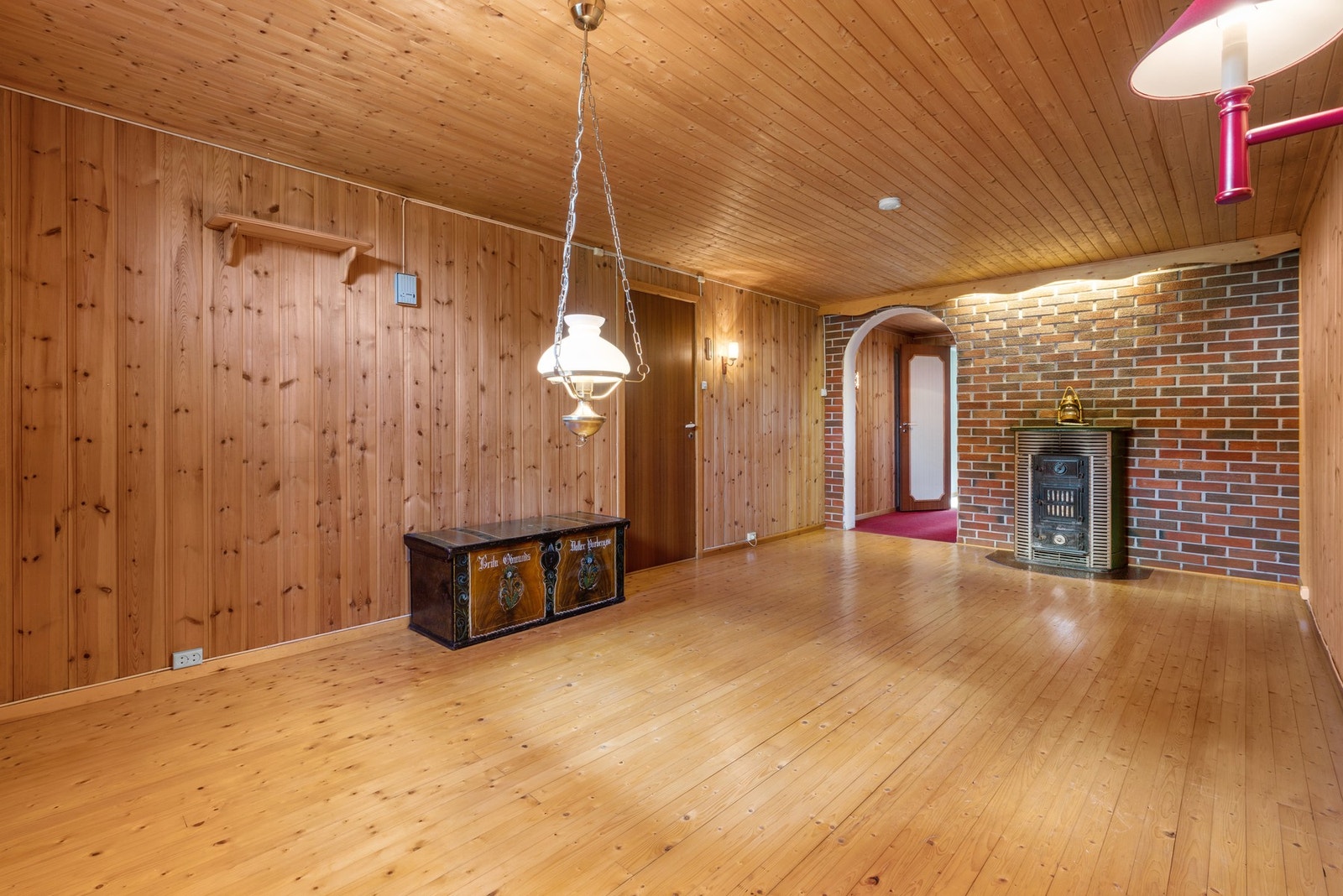 Rommet har panelvegger, tregulv og tak i tre. Det er en peis og en buegang til neste rom. Galleribilde