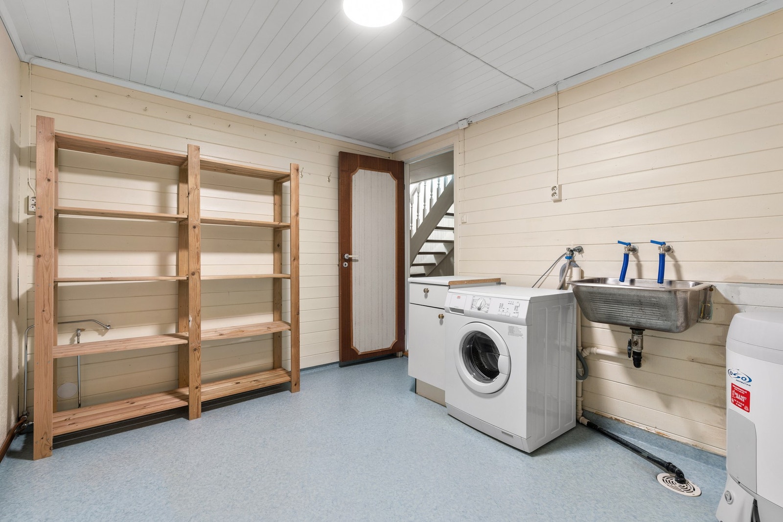 Vaskerom med vaskemaskin, utslagsvask og hyllesystem. Lyse vegger og tak, samt praktisk gulvbelegg. Galleribilde