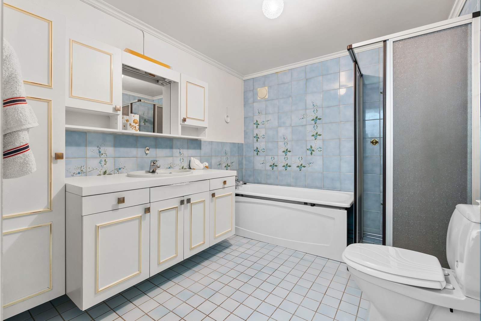 Badet har flislagte vegger og gulv, badekar, dusjkabinett og toalett. Galleribilde