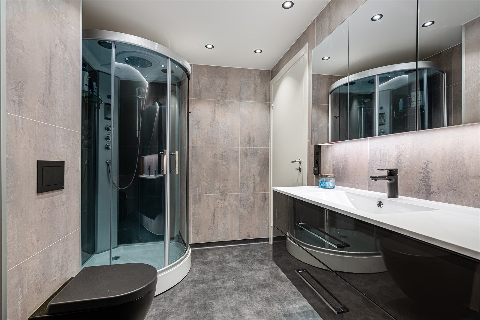 Badet inneholder dusjkabinett, servant med skuffer og skapinnredning, badekar og veggmontert wc. Galleribilde