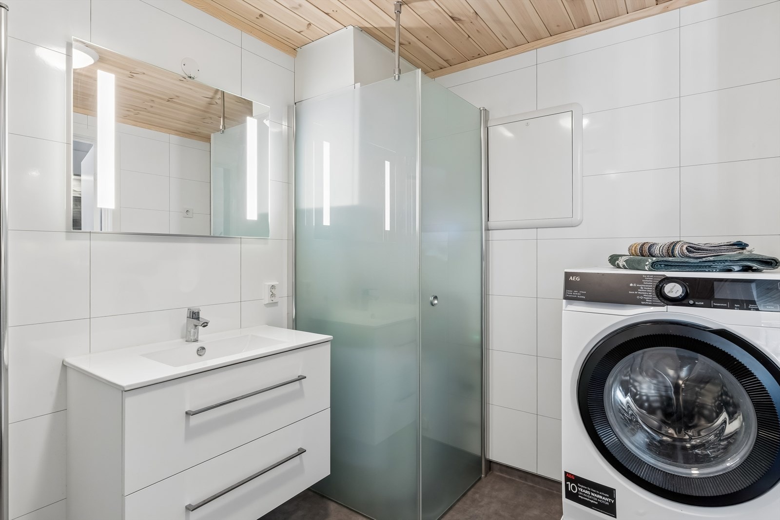 Badet er utstyrt med gulvvarme, baderomsplater på veggene og våtromsbelegg på gulvet. Et stilrent og nøytralt bad. Bak glassveggene har man bla. tekniske installasjoner og varmtvannsberederen. Galleribilde