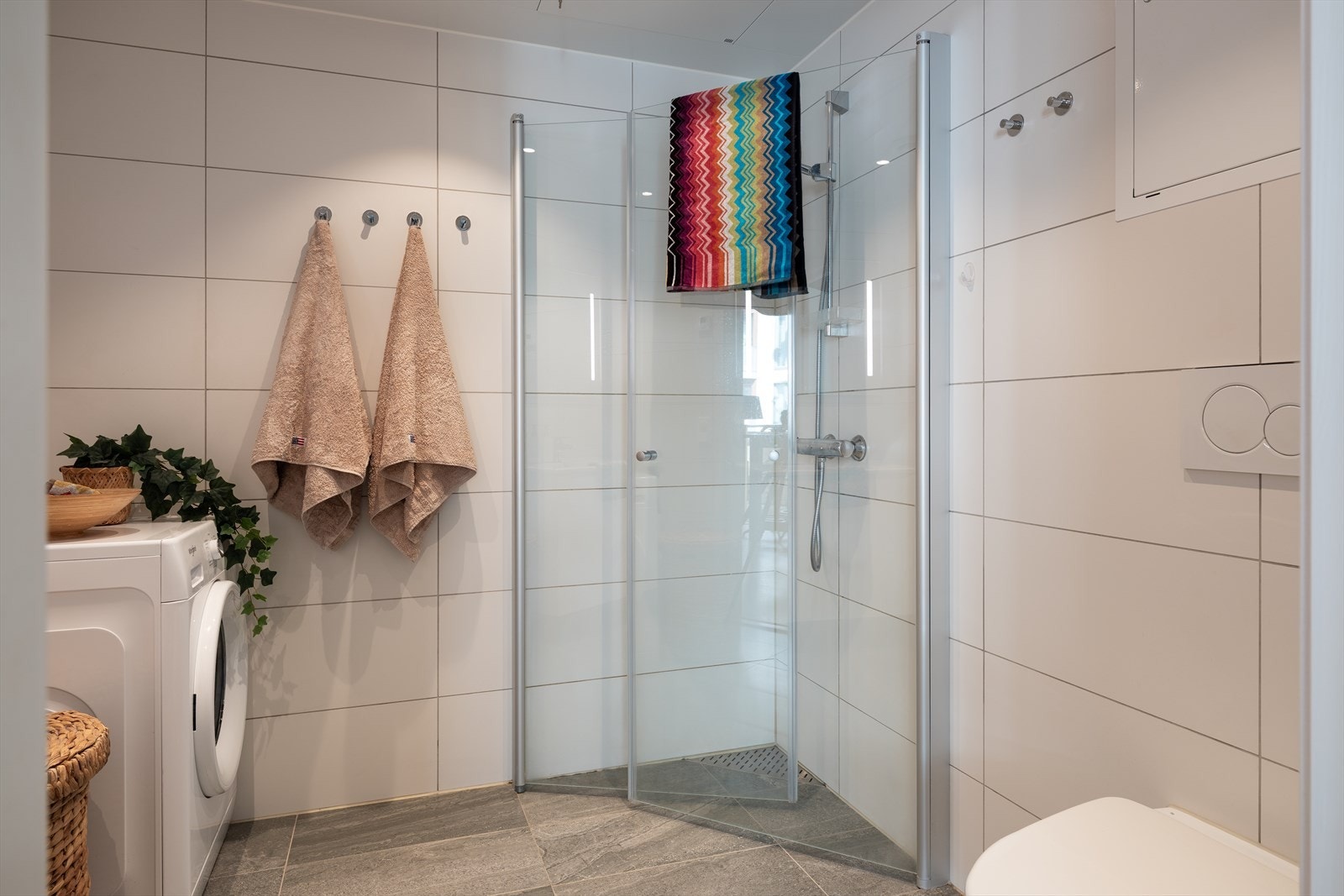 Badet er utstyrt med servant, servantskap, dusjhjørne med dører, vegghengt toalett og opplegg for vaskemaskin. Galleribilde