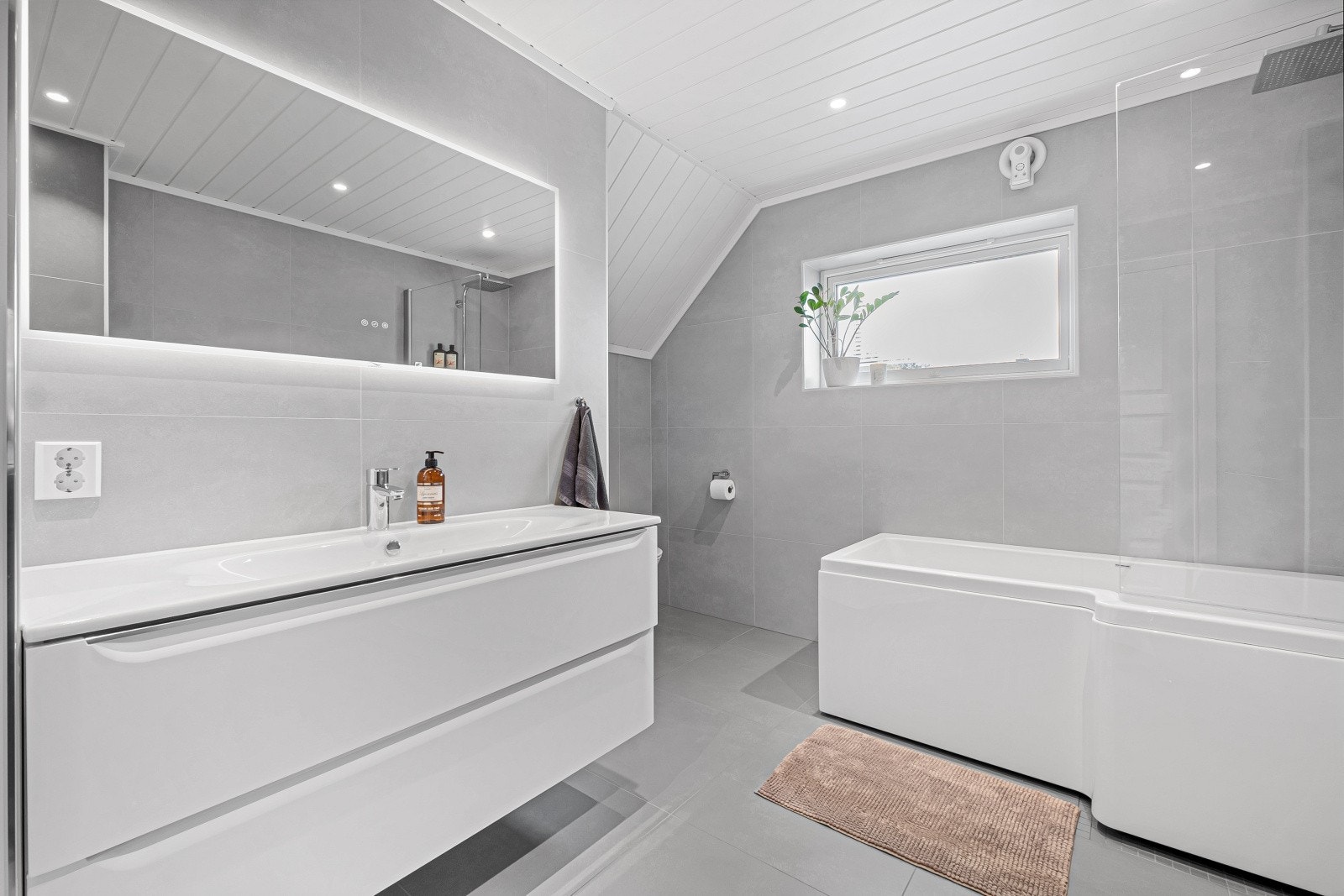 Badet er innredet med en pen baderomsinnredning med heldekkende servant nedfelt i skuffeseksjon, samt speil med integrert belysning som gir et elegant og praktisk uttrykk. Galleribilde