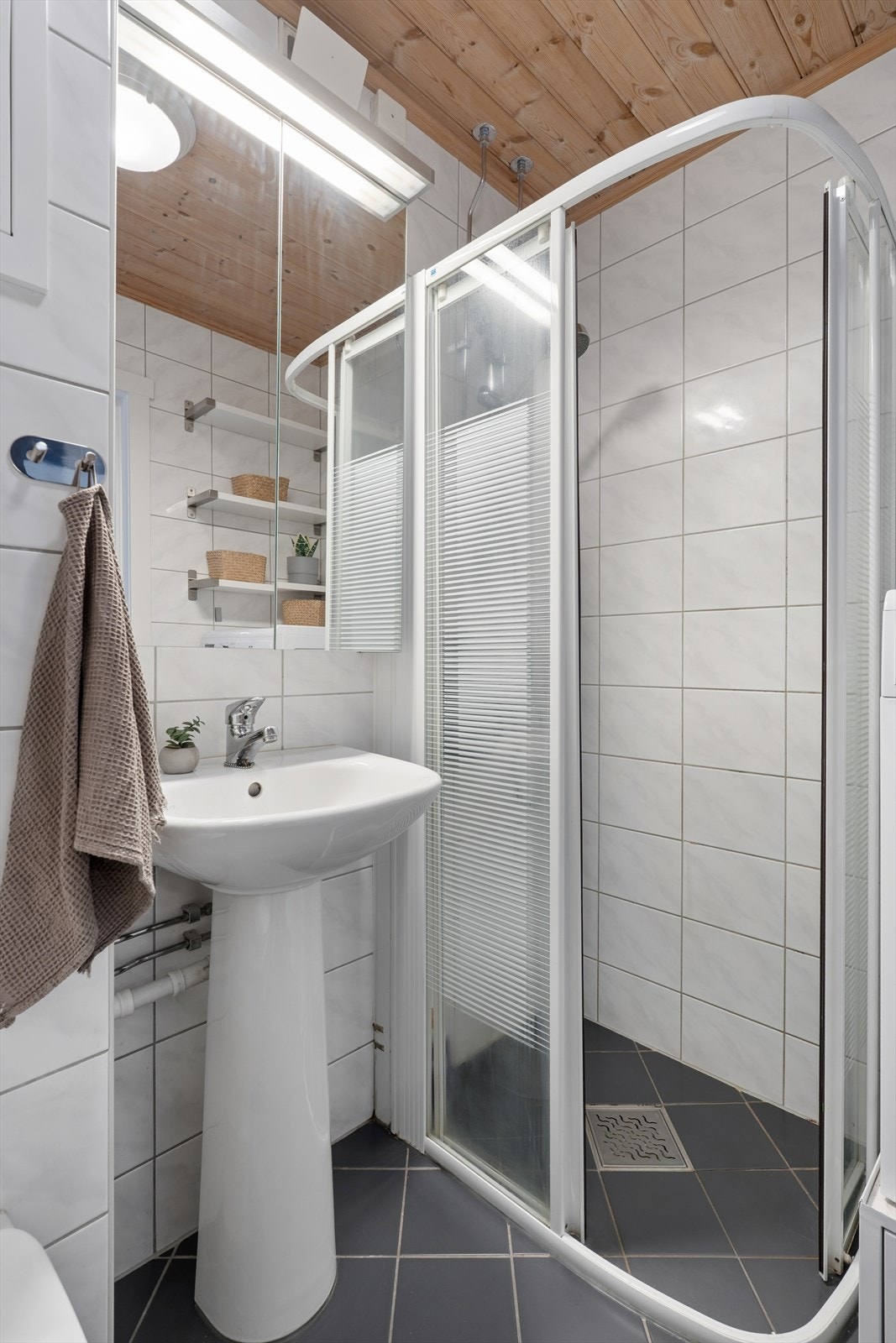 Badet er utstyrt med dusjhjørne, vegghengt toalett, opplegg for vaskemaskin og enkel servantinnredning. Galleribilde