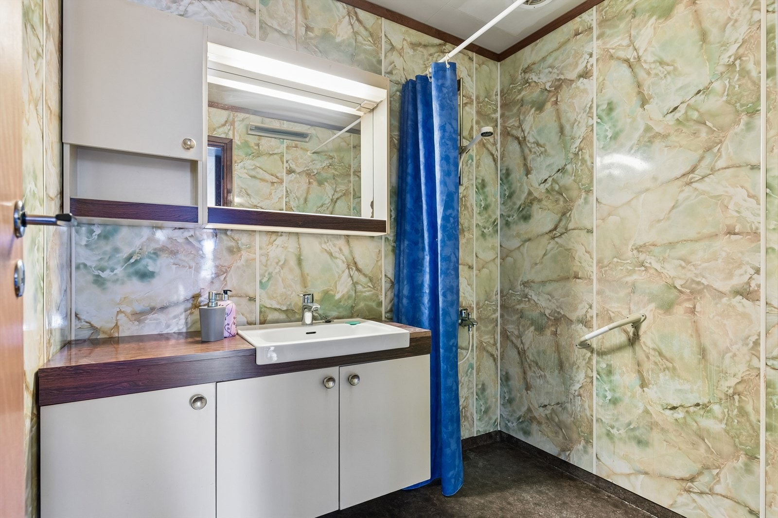 Badet i den opprinnelige boligen har vinylbelegg på gulv, baderomsplater og servantinnredning. Galleribilde