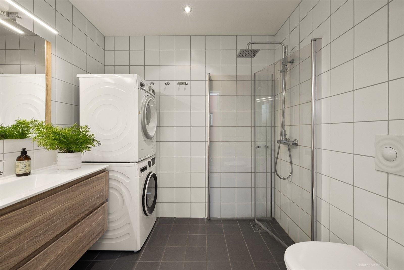 Badet er flislagt og utstyrt med varme i gulvet, vegghengt toalett og opplegg for vaskesøyle. Galleribilde