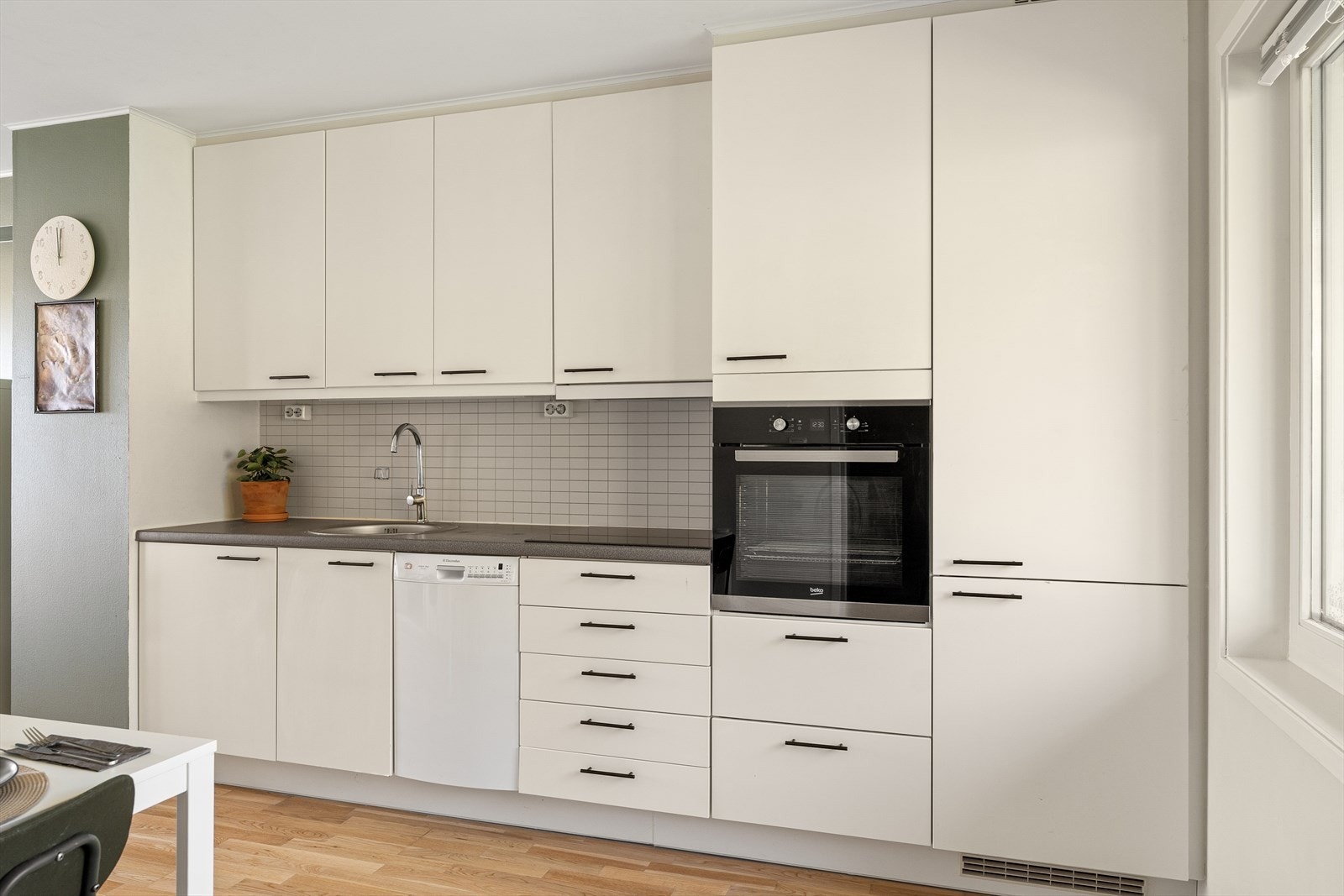 Kjøkkeninnredningen har hvite, glatte fronter og integrerte hvitevarer. Laminatbenkeplaten er slitesterk og godt egnet for matlaging. Galleribilde
