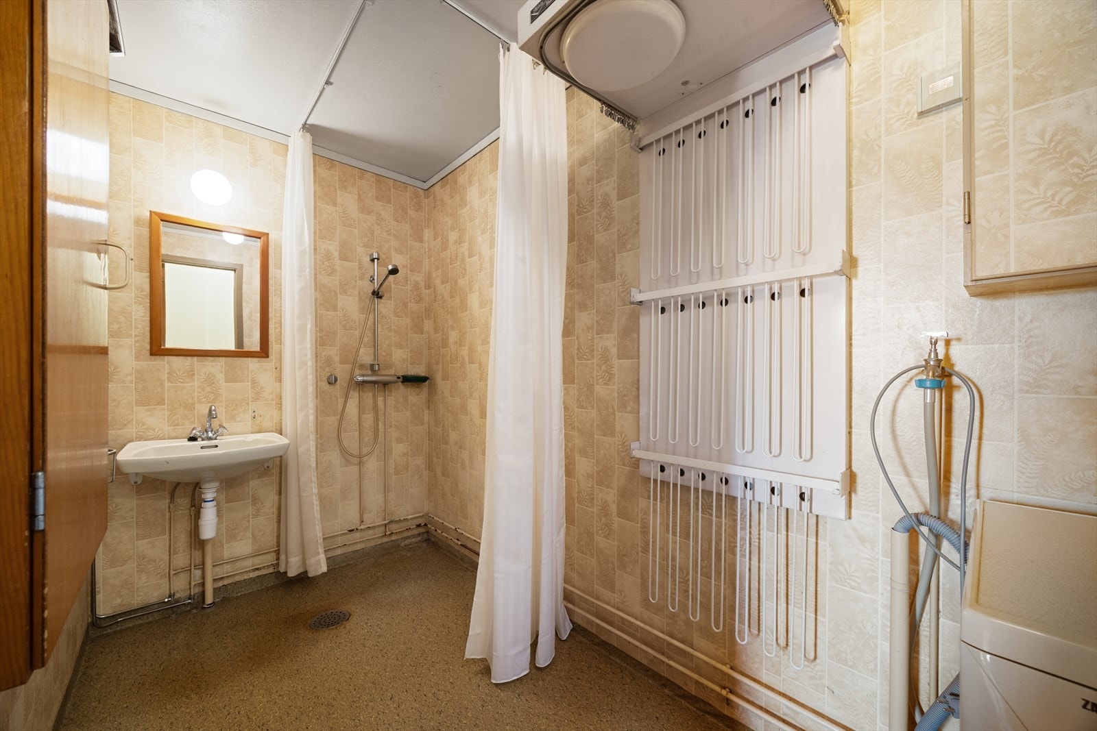 Romslig bad av eldre standard. Badet er utstyrt med vegghengt vask, opplegg for vaskemaskin og åpen dusj med forheng. Galleribilde