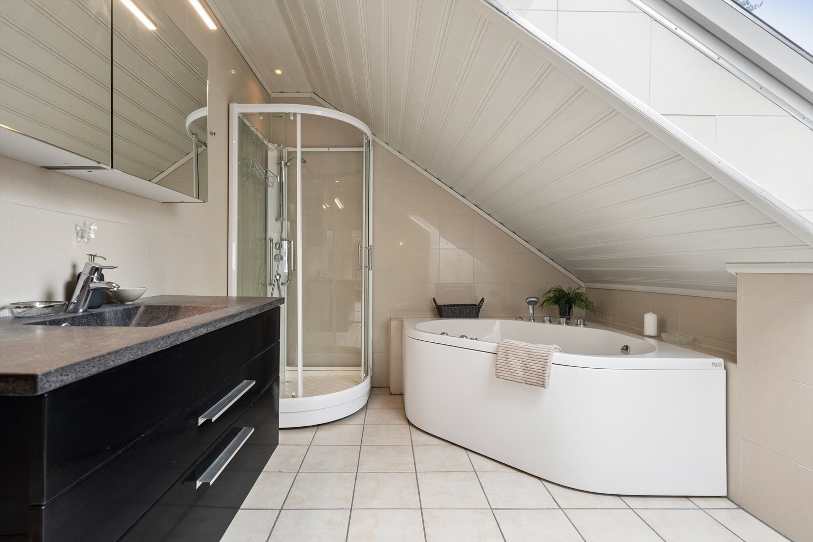 Badet er fra 2006 og er innredet med lyse fliser på gulv og vegger og har varmekabler. Badet er ellers utstyrt med dusjkabinett, hjørnebadekar, vegghengt toalett, bidé og baderomsinnredning med nedfelt servant. Galleribilde