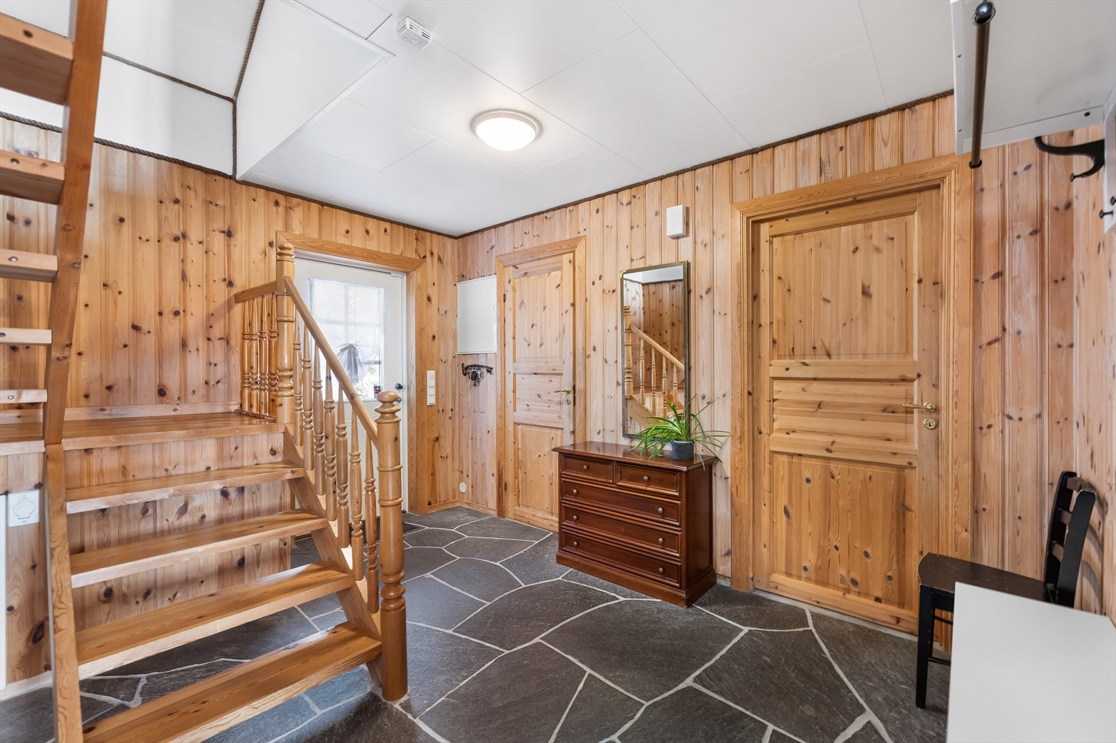 En innbydende hall med slitesterkt bruddskifer på gulvet. Den lakkerte tretrappen binder etasjene sammen. Galleribilde