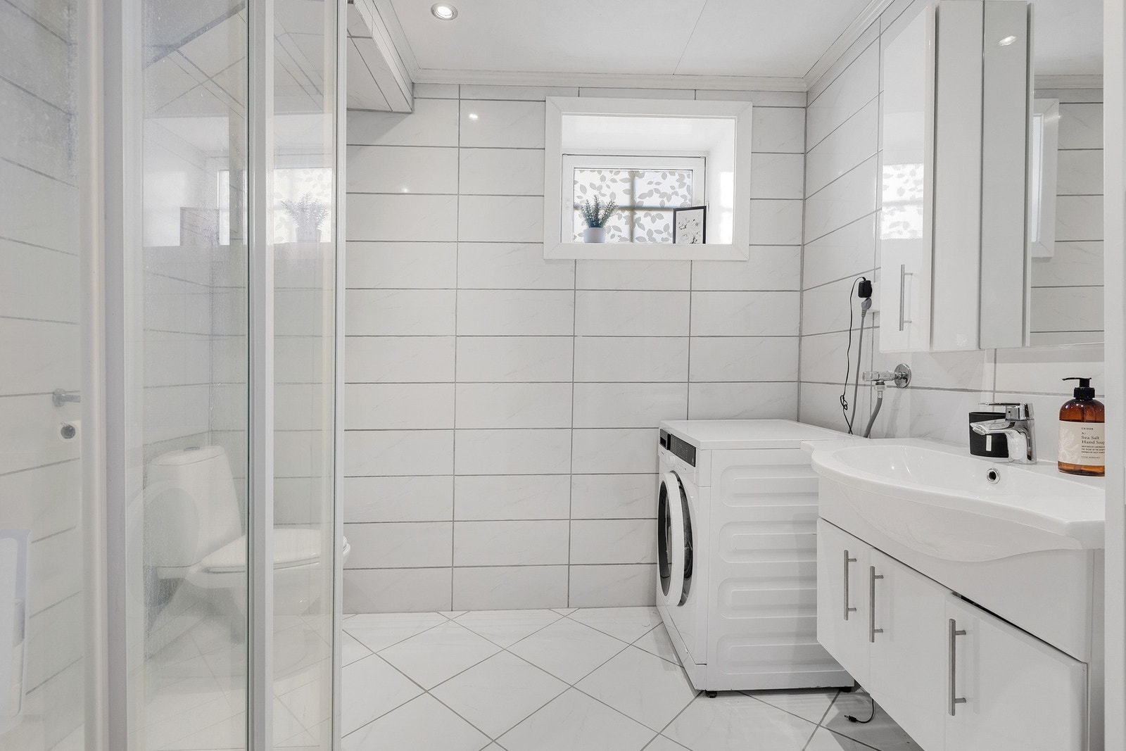 Badet i kjelleretasjen har også flislagte gulv og vegger, samt himlingsplater. Opplegg for vaskemaskin, baderoms innredning med nedfelt servant, speil og belysning. Galleribilde