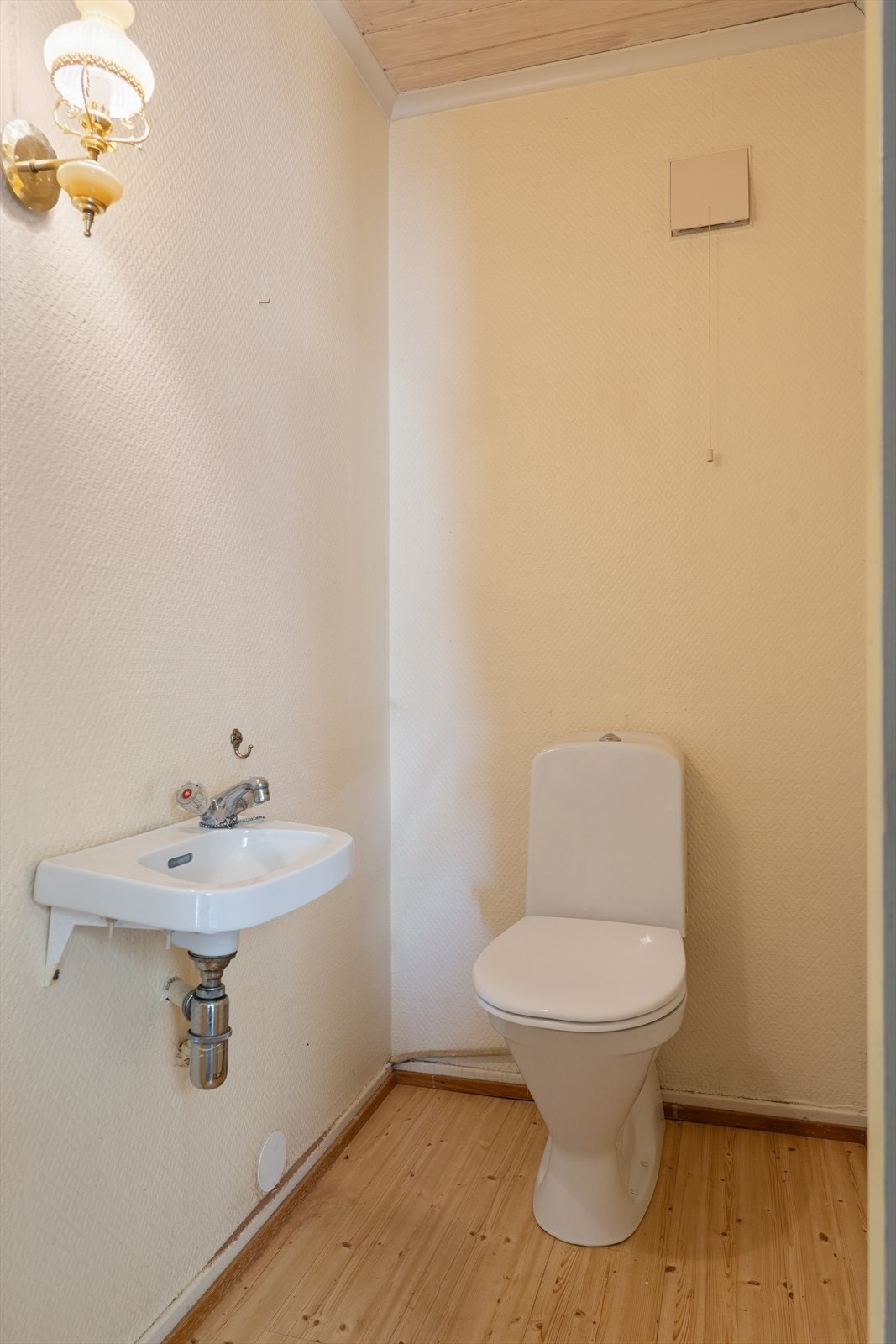 Toalettrom i 1. etasje med laminatgulv, malt strietapet på vegg og panel i himlingen. Inneholder servant og wc, sistnevnte byttet i senere år. Galleribilde