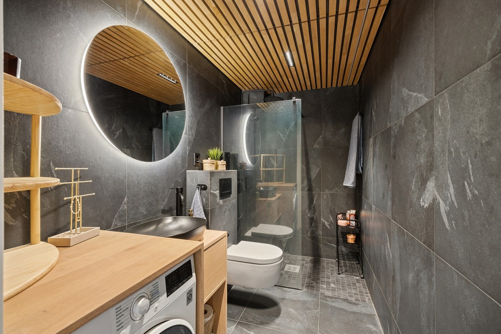 Badet er praktisk innredet med dusjhjørne, vegghengt toalett og plass til vaskemaskin, samt gode oppbevaringsmuligheter i innredningen. Galleribilde