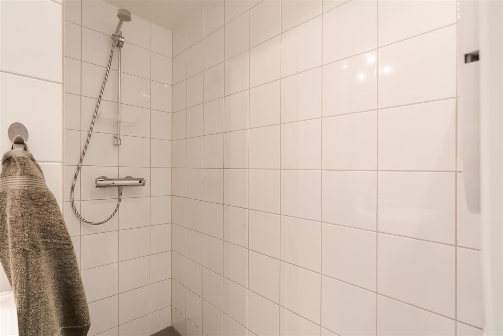 Downlights og gulvvarme er installert, og badet har vegghengt toalett, opplegg for vaskemaskin og en åpen dusjnisje. Den øvrige innredningen består av servant med sorte underskuffer og et speil med belysning. Galleribilde