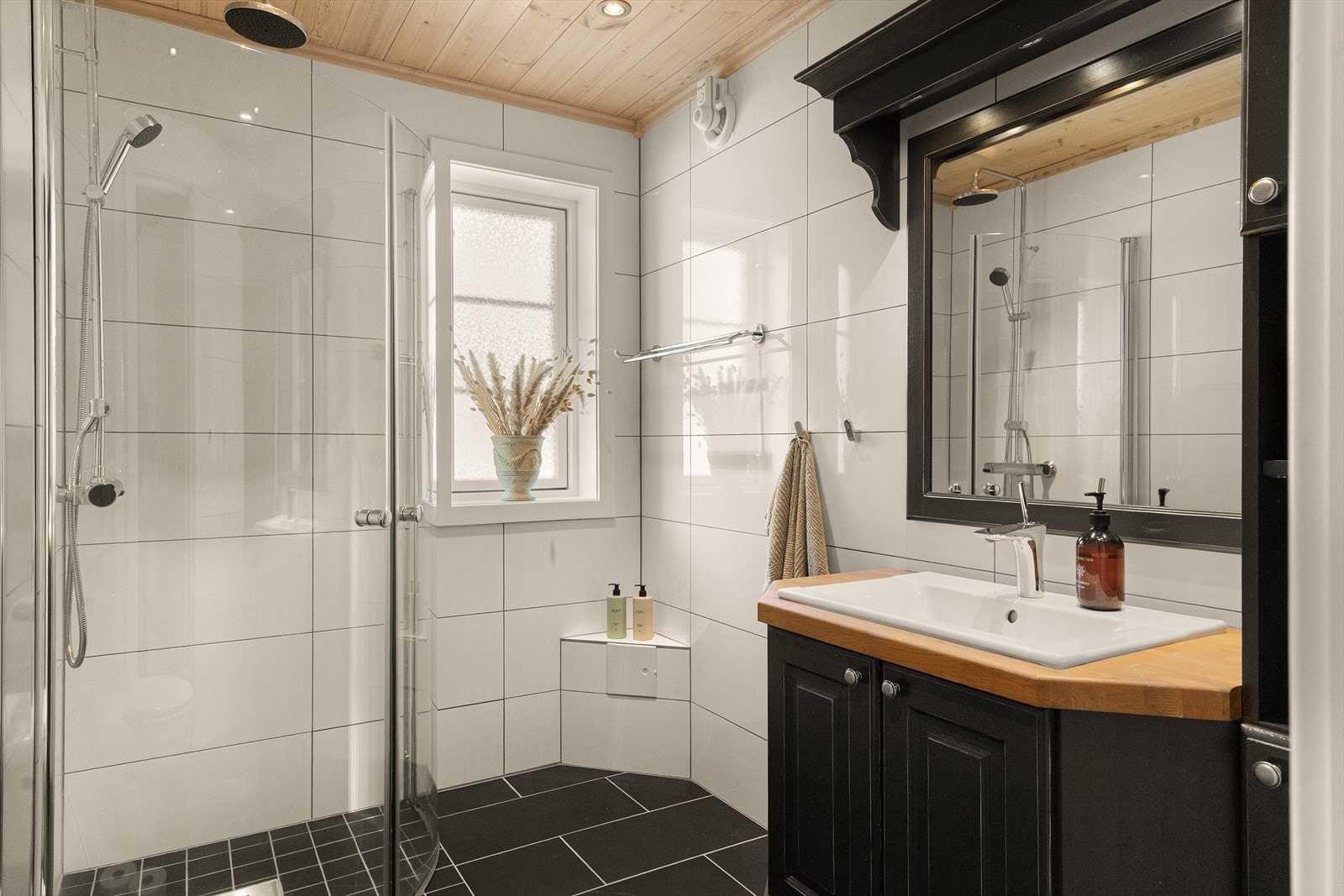 Badet er pent og romslig, innredet med vegghengt toalett, dusjhjørne og servant med stilren innredning Galleribilde