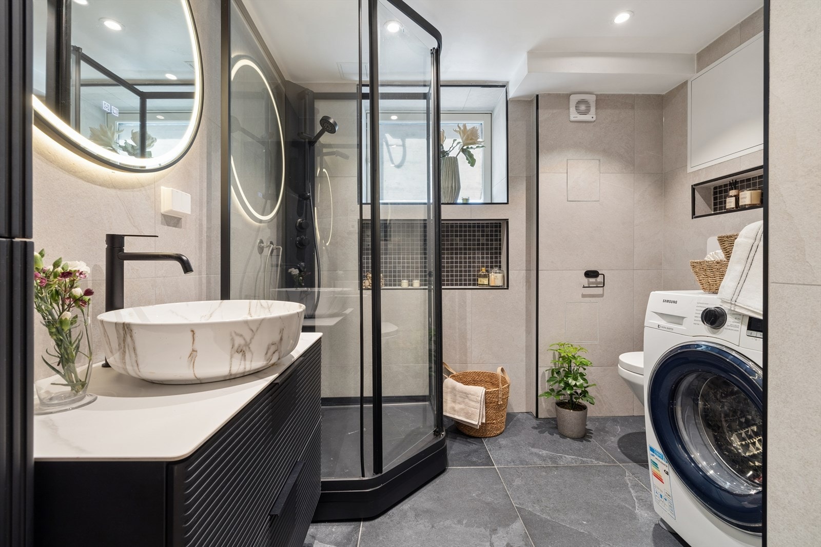 badet har en stilren utforming med flislagte overflater og varmekabler i gulvet for ekstra komfort. Rommet er bla.a innredet med dusjkabinett, servant, vegghengt toalett med innebygget sisterne samt opplegg for vaskemaskin. Galleribilde