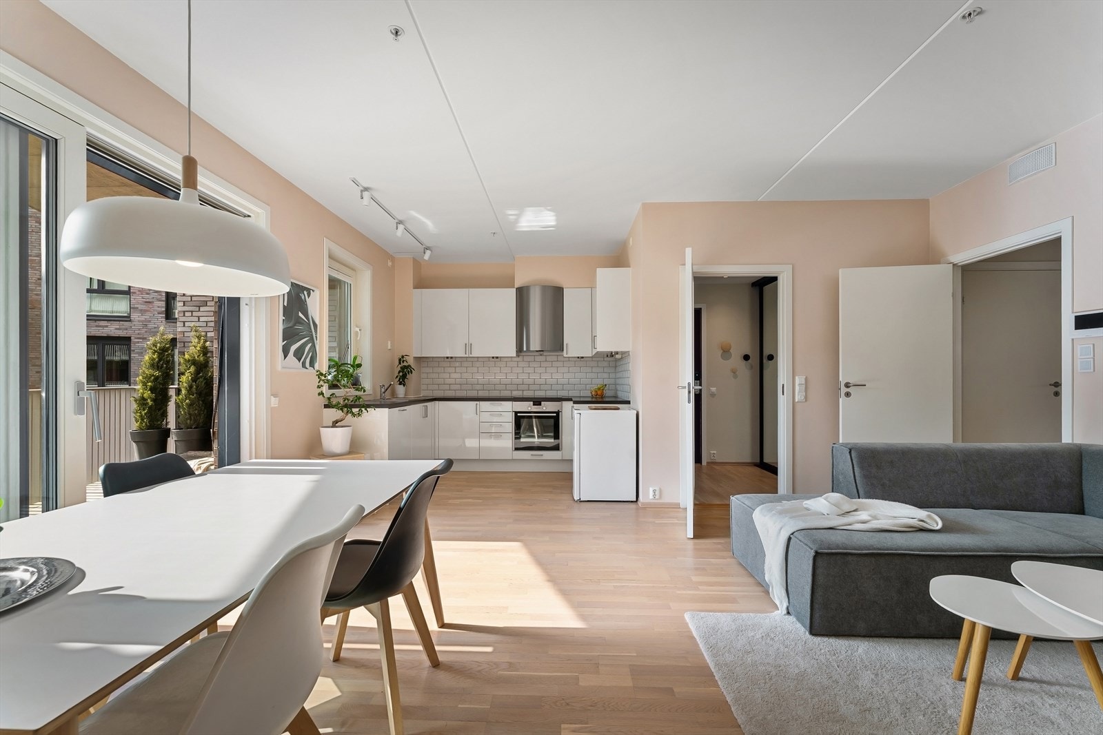 Kjøkkenet har innredning fra byggeår med hvite, glatte fronter, fliser på vegg over kjøkkenbenk og benkeplate i laminat. Galleribilde