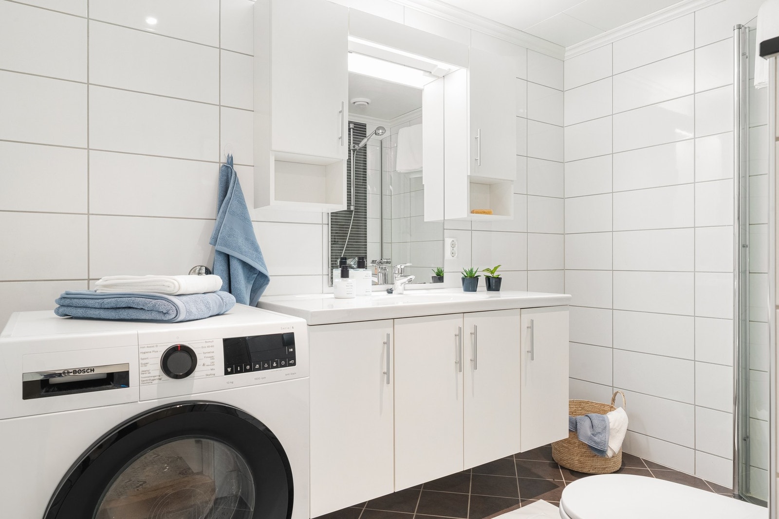 Badet er innredet med baderomsinnredning med nedfelt servant, vegghengt toalett, dusjhjørne og opplegg for vaskemaskin. Galleribilde